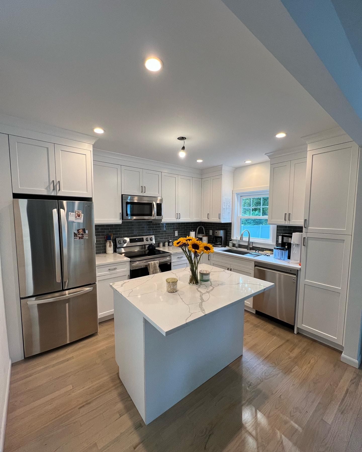 Bright modern kitchen with stainless appliances, white cabinets, and a marble island with flowers.