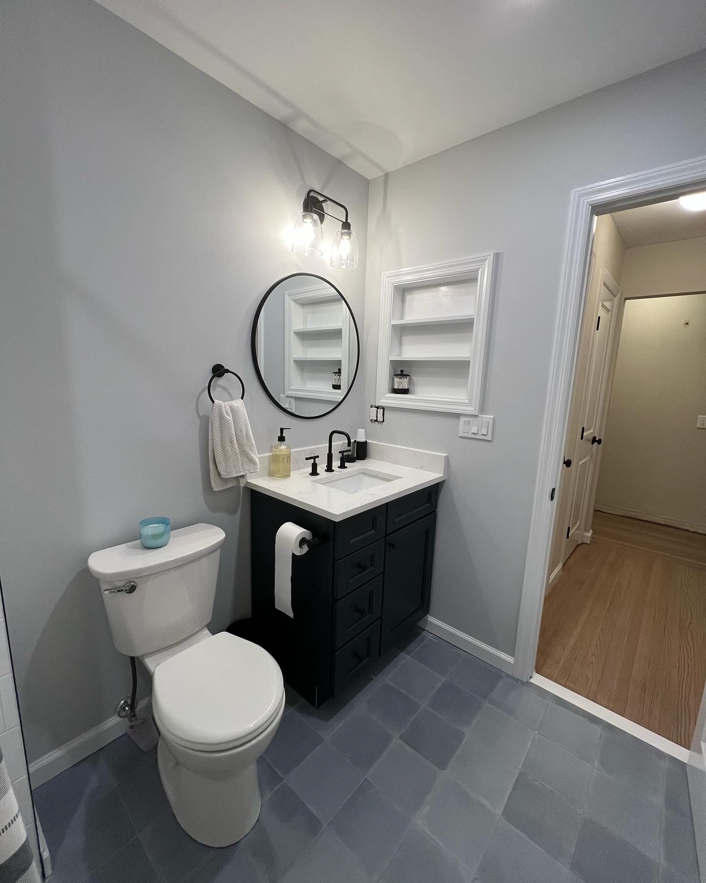 Small bathroom with toilet, vanity sink, mirror, and gray tile floor; doorway to hall on right
