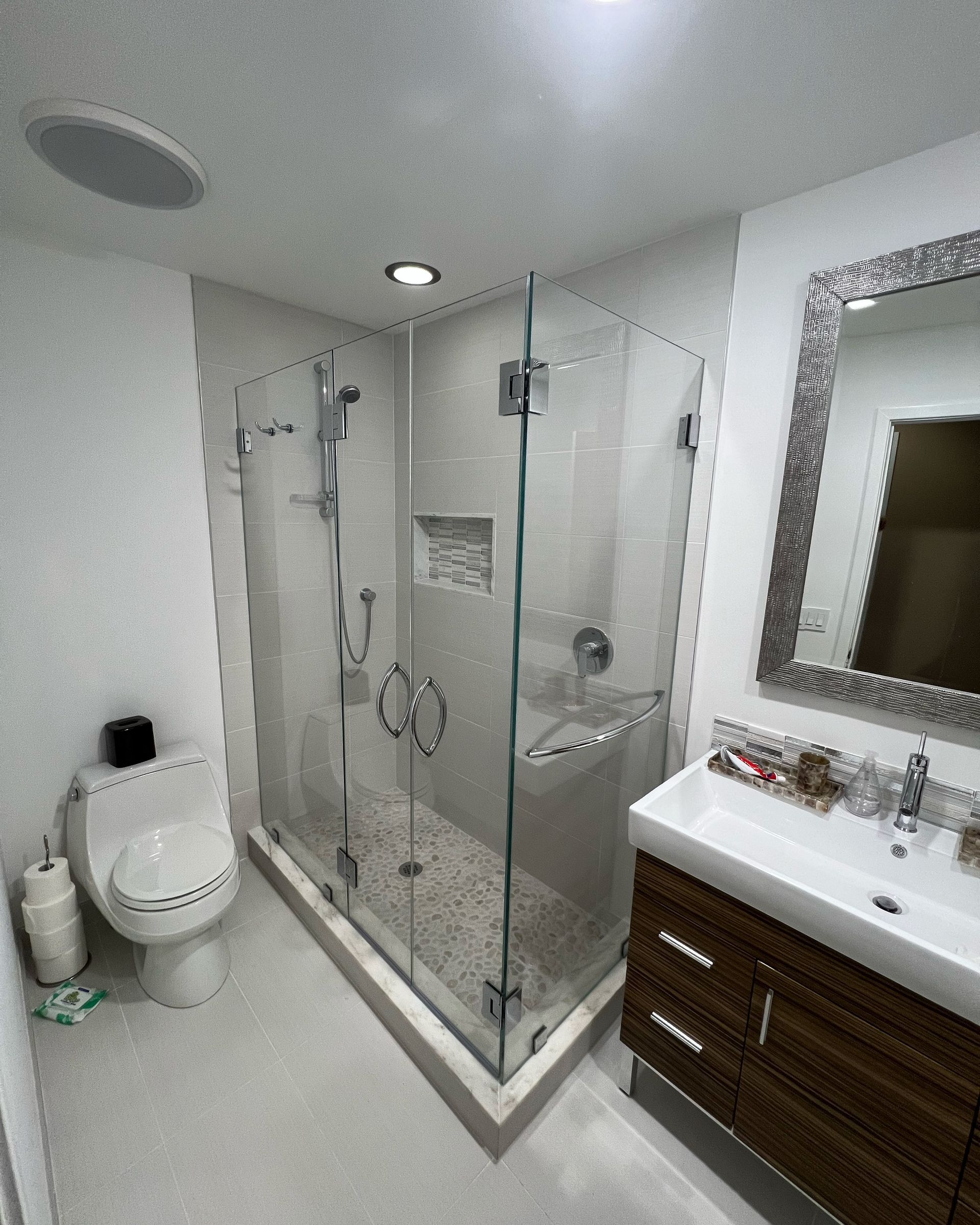 Modern bathroom with glass shower, toilet, vanity, and large mirror, in white and dark wood tones