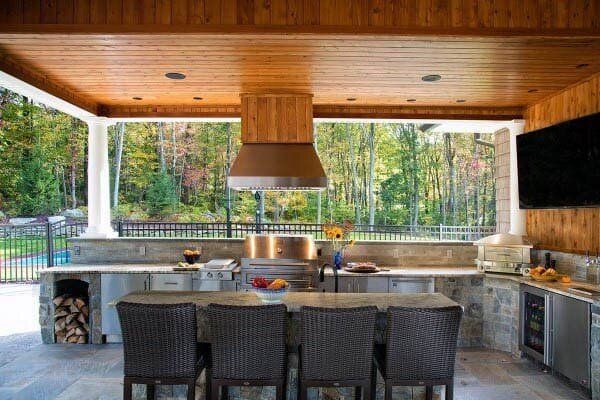 A large outdoor kitchen with a table and chairs and a grill.