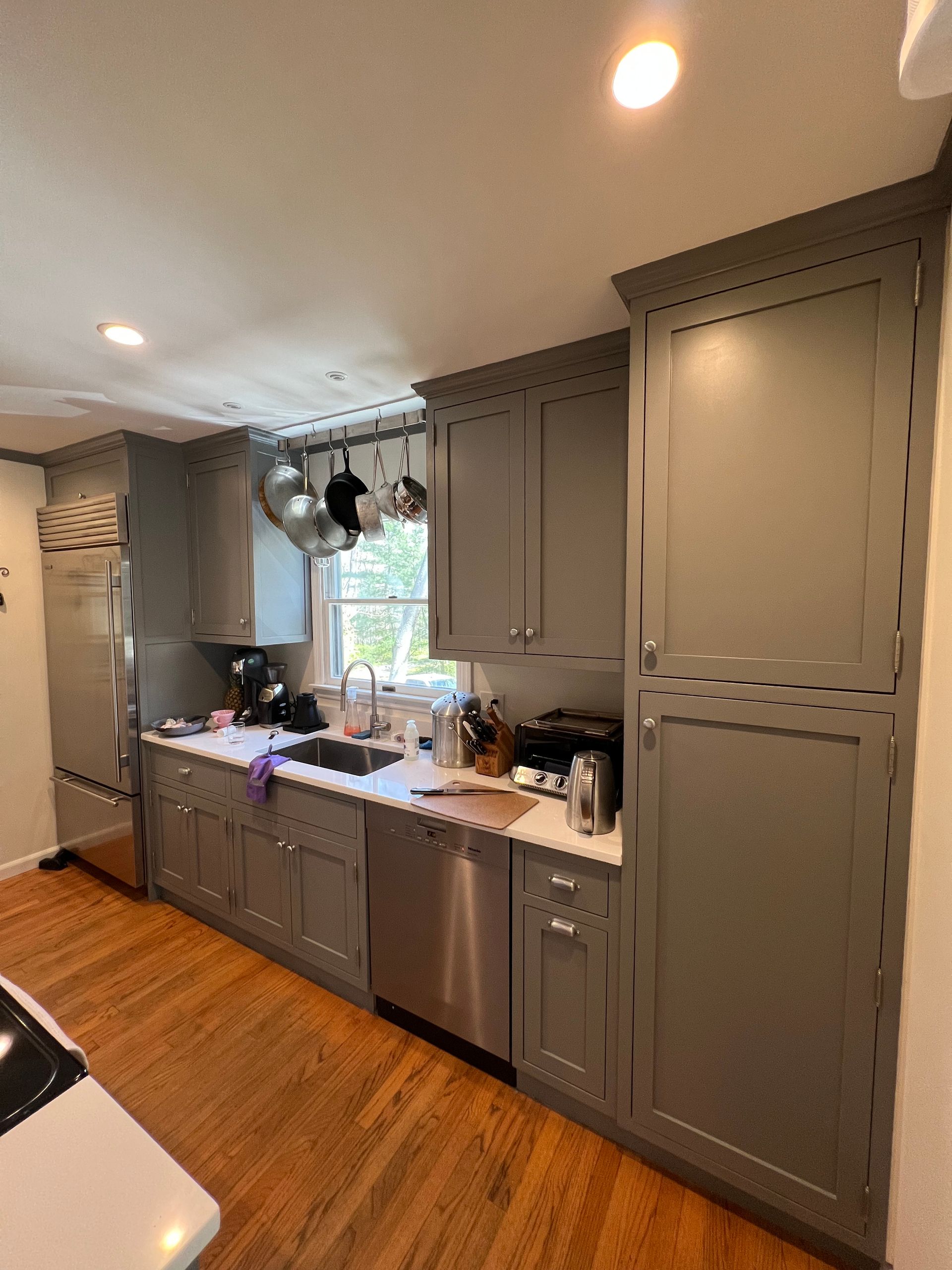 Modern kitchen with gray cabinets, wood floor, white countertops, and a window over the sink