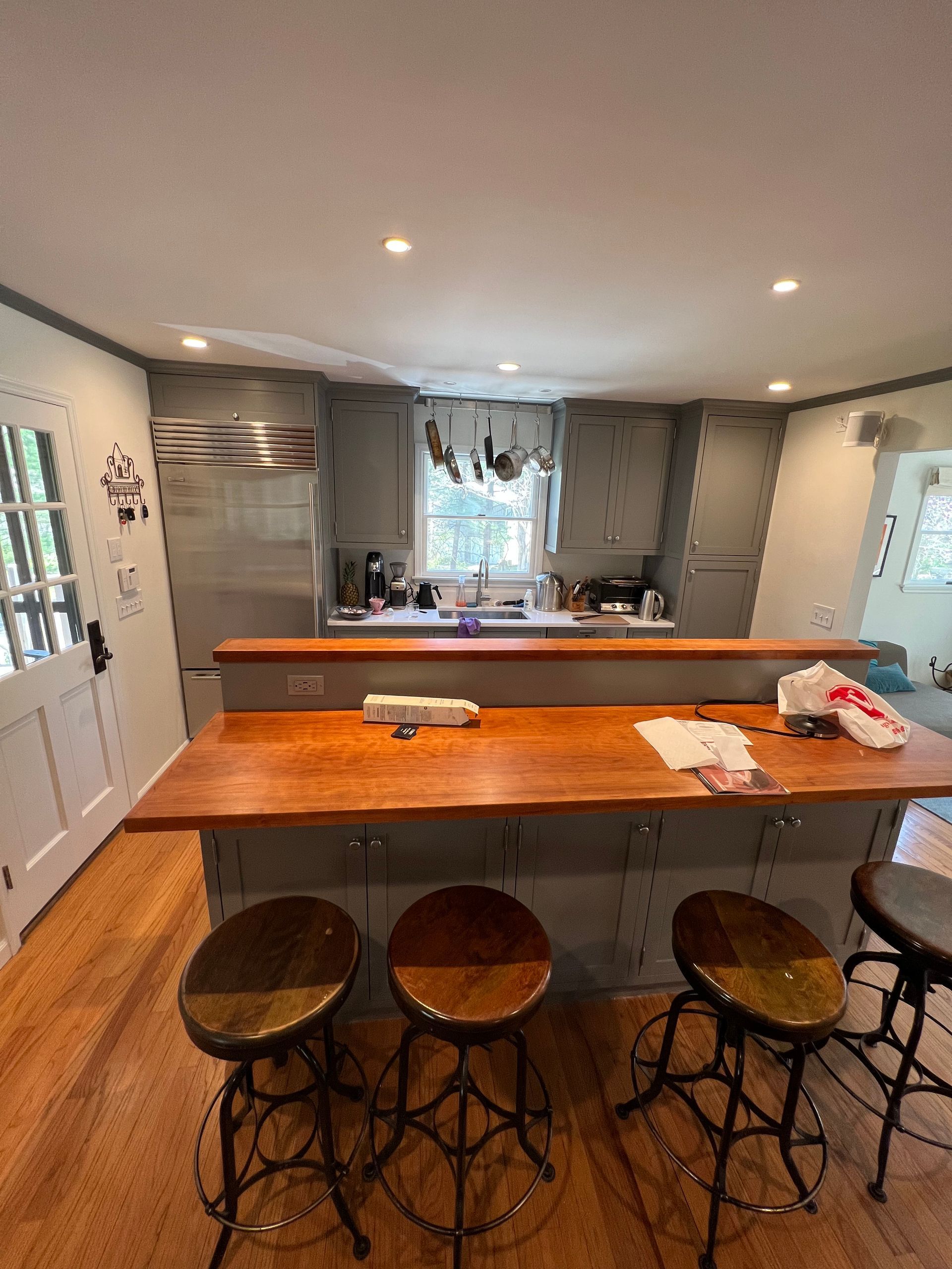 Modern kitchen with wooden island, three stools, gray cabinets, and a bright window over the sink.
