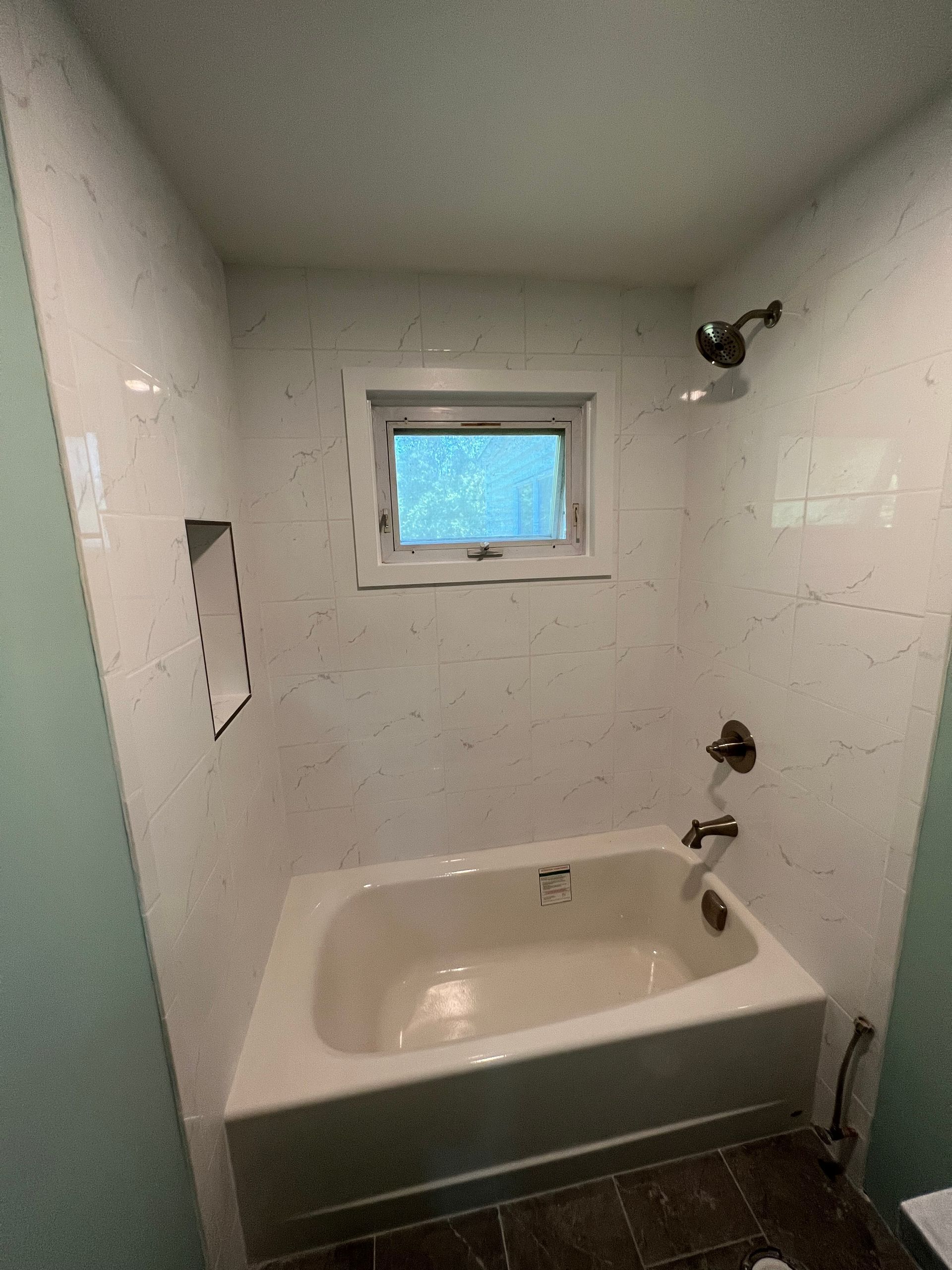 Small bathroom with a white bathtub, tiled walls, and a tiny frosted window.