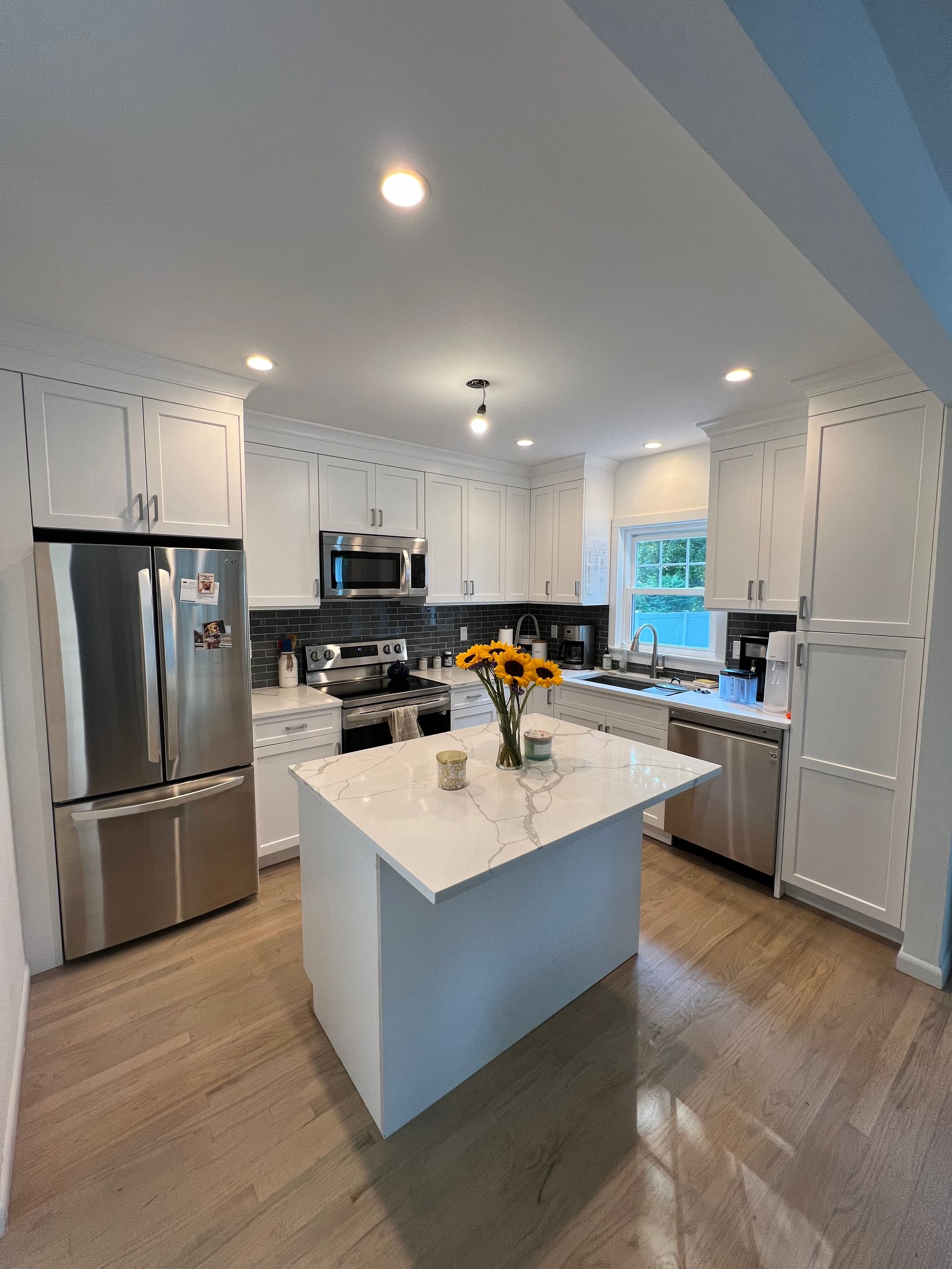Bright modern kitchen with white cabinets, stainless appliances, and a marble island with flowers