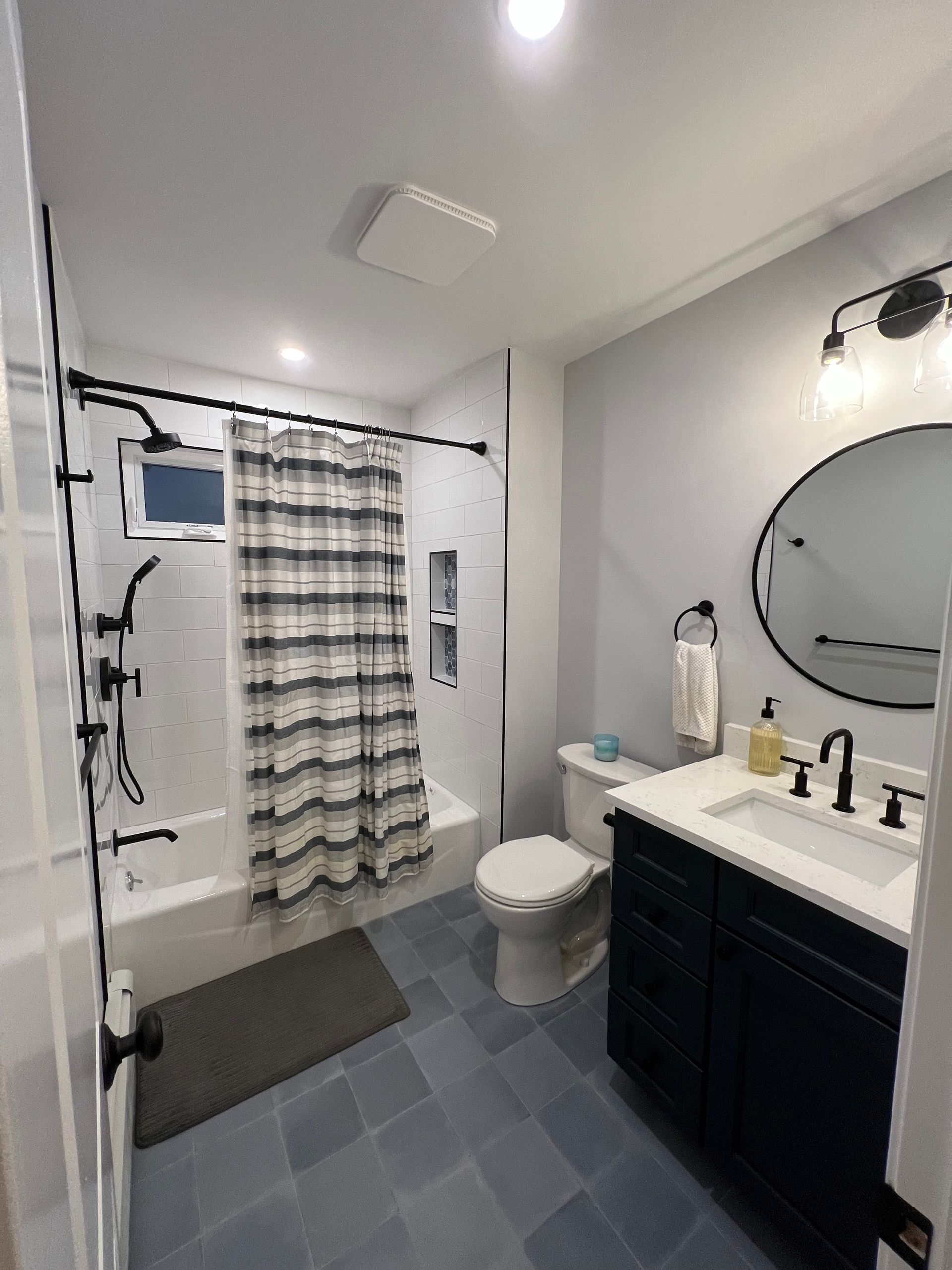 Small modern bathroom with a shower curtain, toilet, vanity sink, and round mirror.