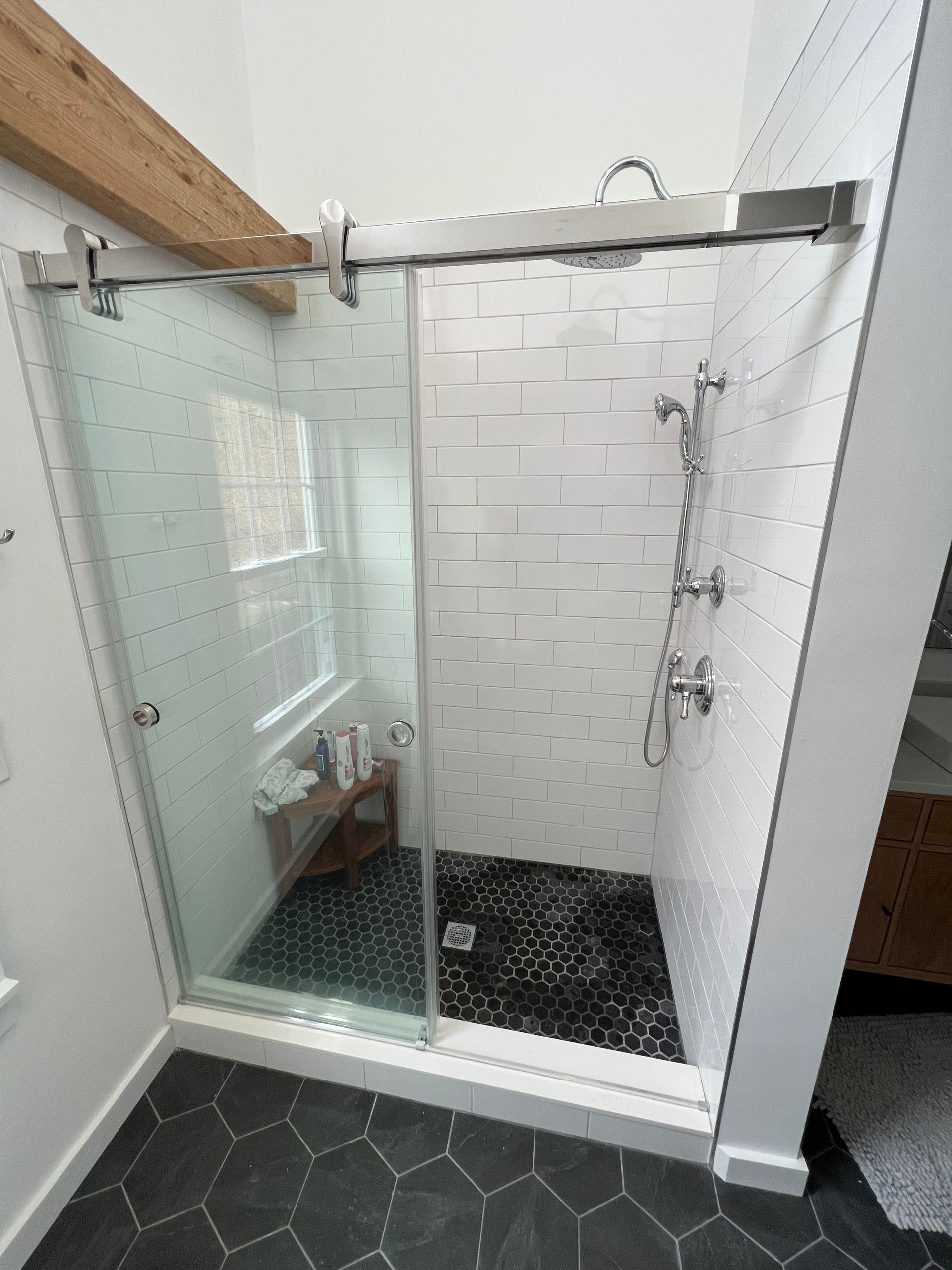 Glass walk-in shower with white subway tile, black shower floor, and gray hexagon bathroom floor