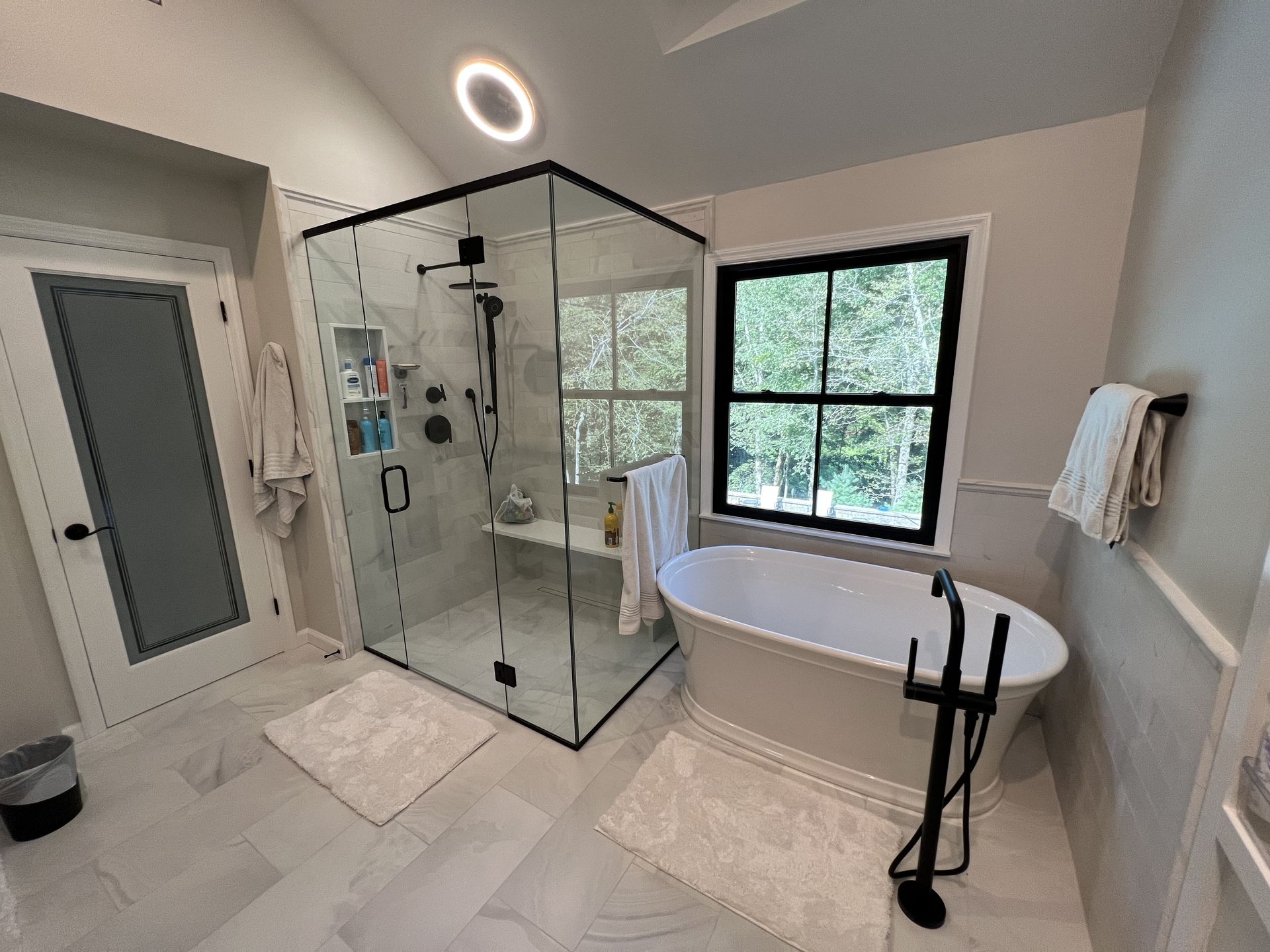 Spacious bathroom with glass shower, soaking tub, and a window with trees in the background.