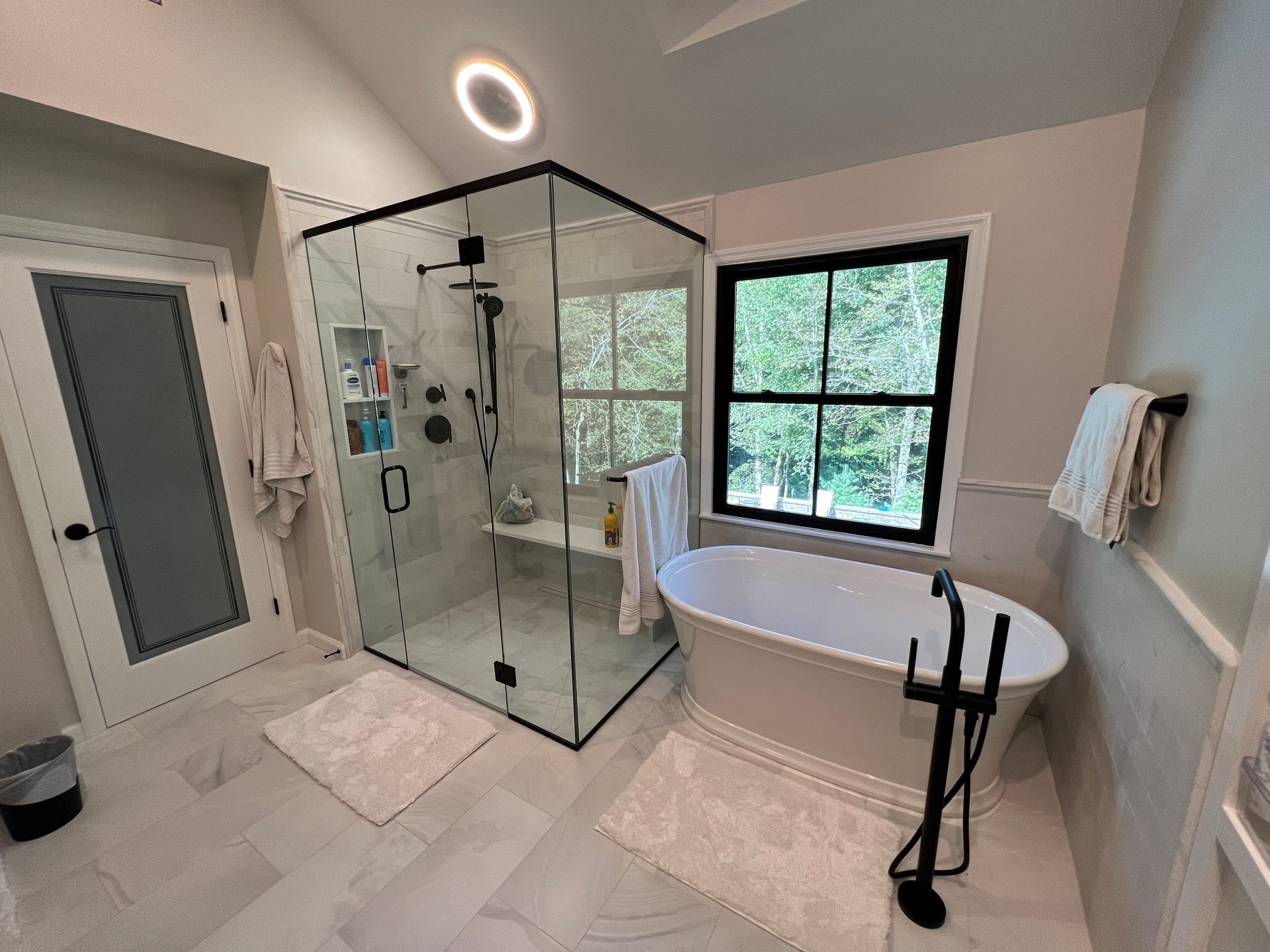 Modern bathroom with glass shower, freestanding tub, vanity, and window light