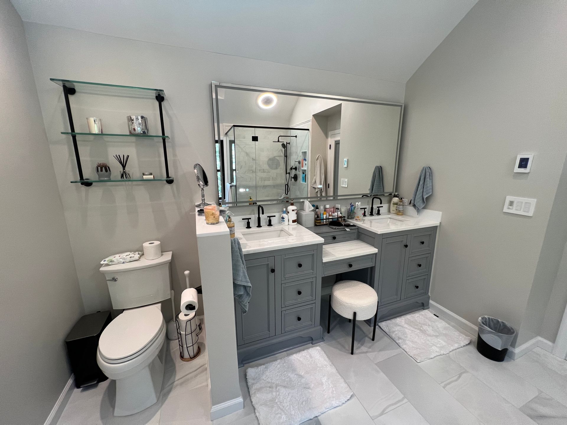 Modern bathroom with double vanity, toilet, large mirror, white tile floor, and gray walls