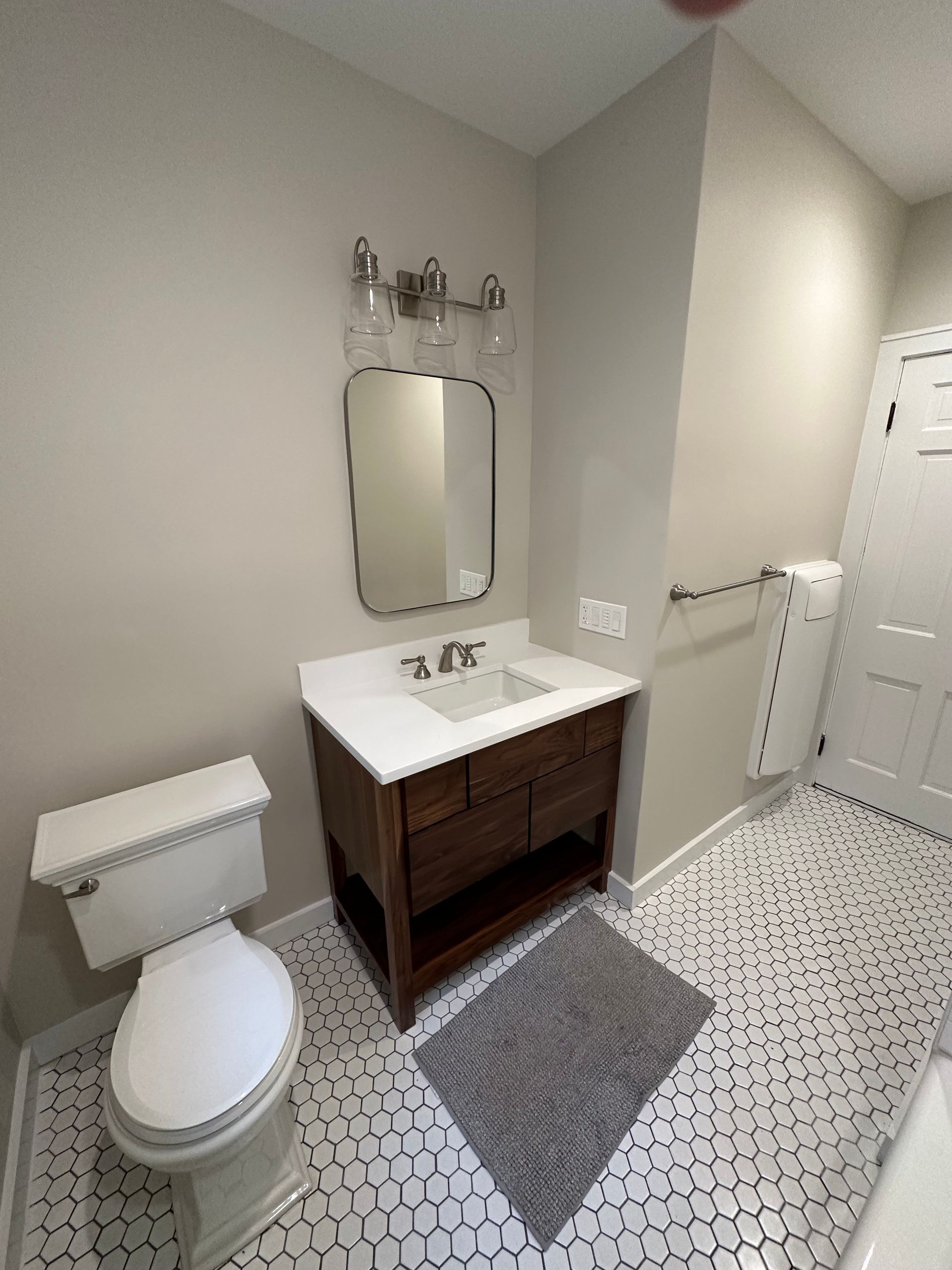 Small bathroom with toilet, sink vanity, mirror, and patterned tile floor.