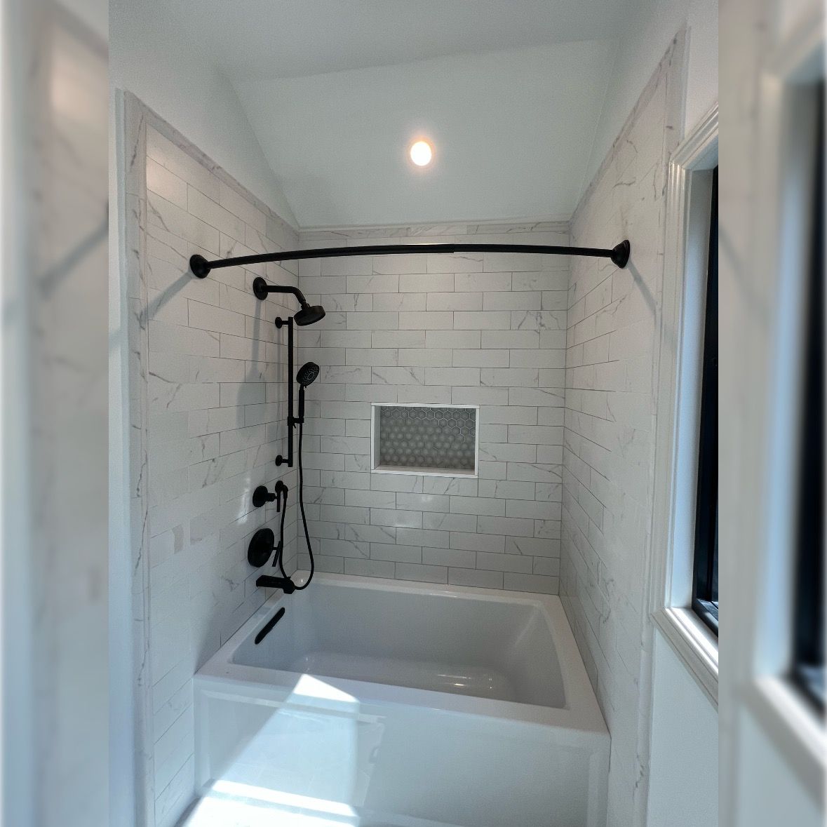 Walk-in shower with white tile, black fixtures, and a tub inset beneath a showerhead