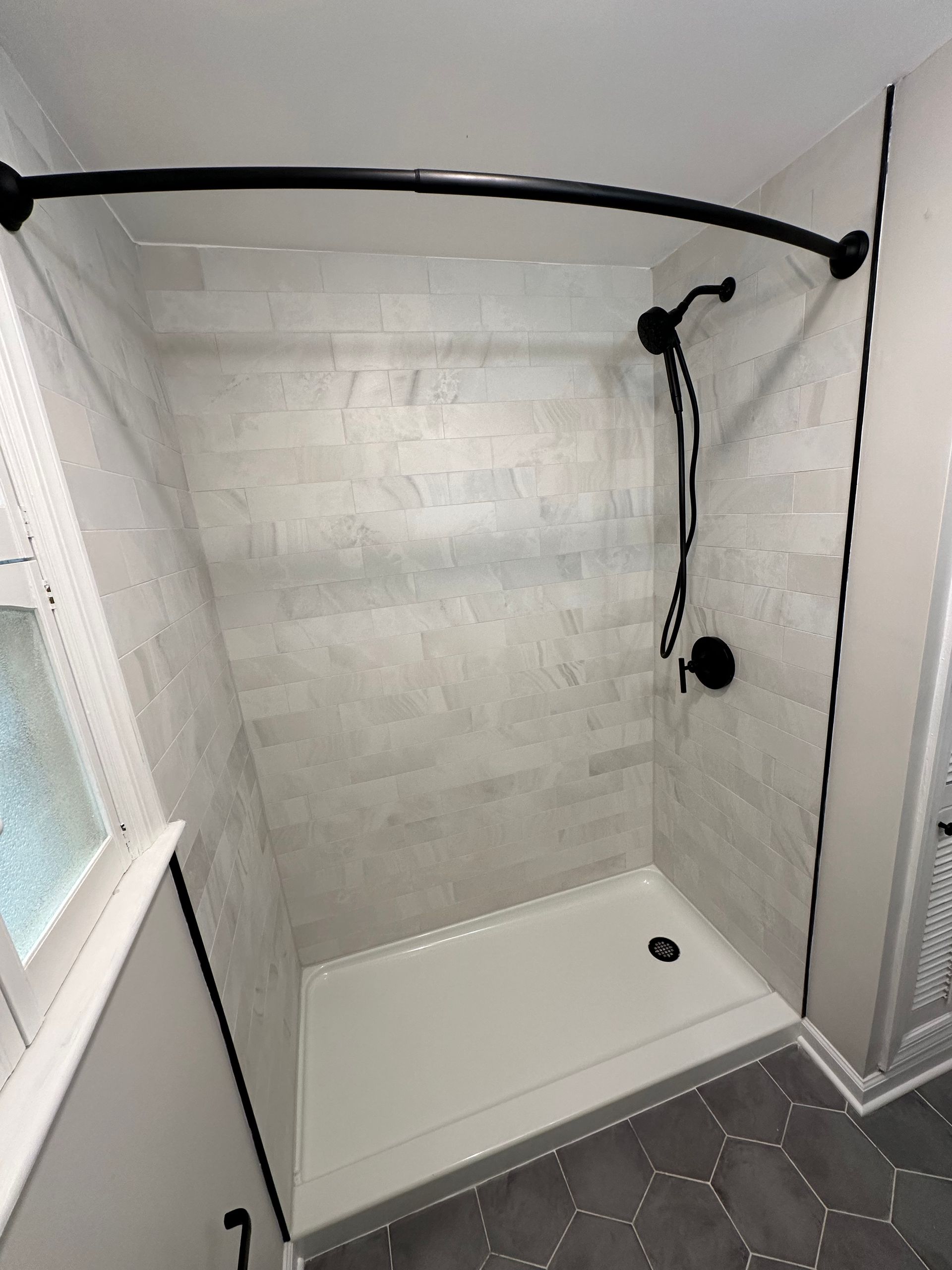 Compact white shower stall with black grab bar and handheld showerhead inside a bathroom