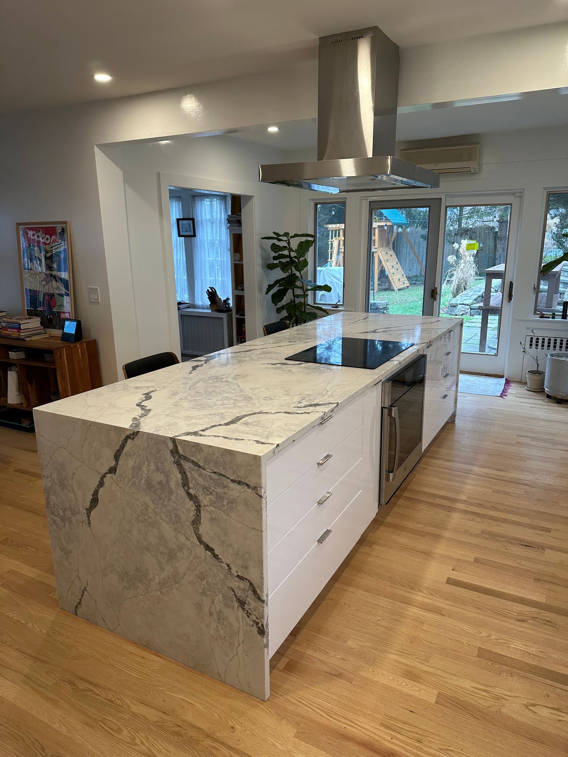 Modern kitchen with large marble island, white cabinets, stainless hood, and glass doors to patio.