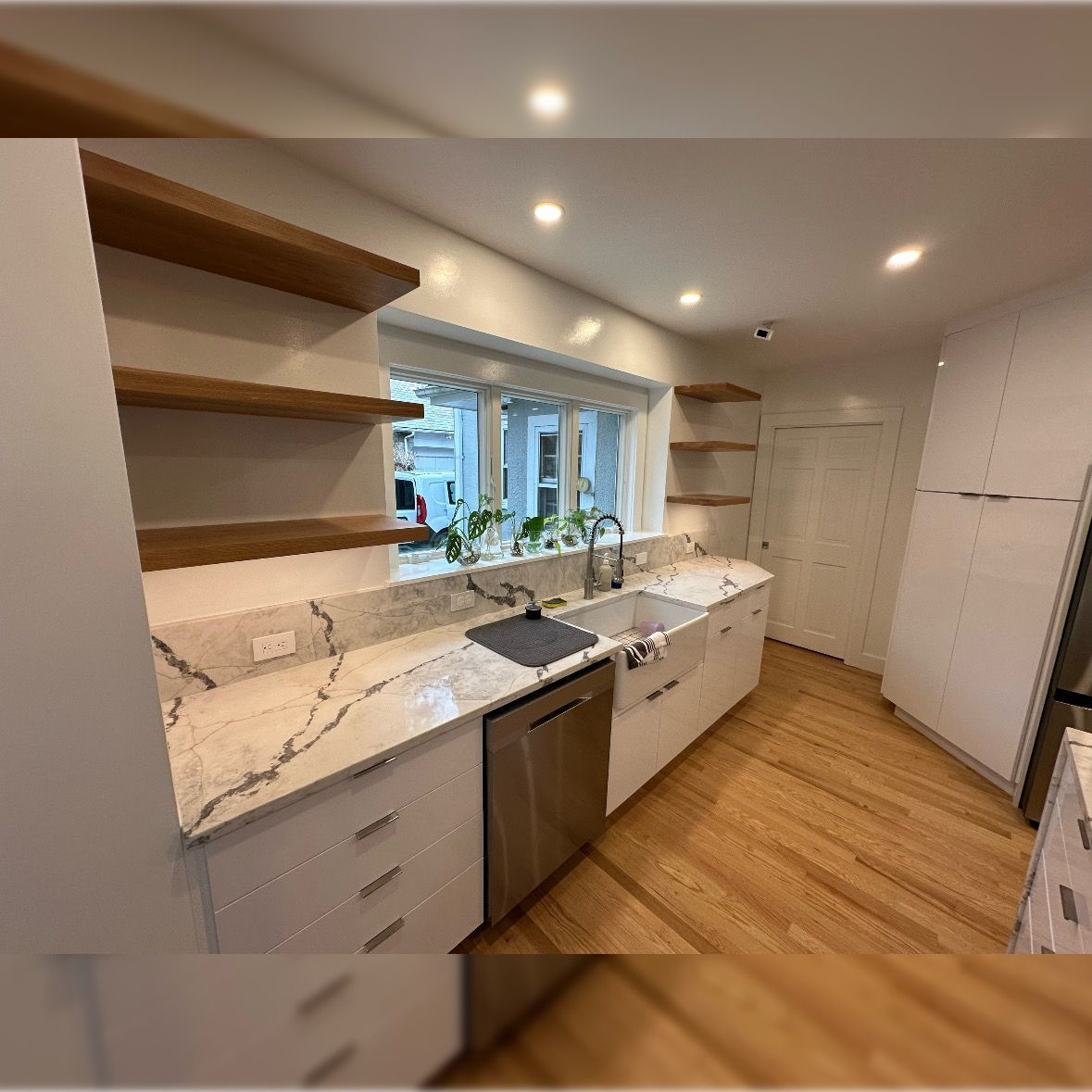 Modern kitchen with white cabinets, wood shelves, marble countertops, and a window over the sink