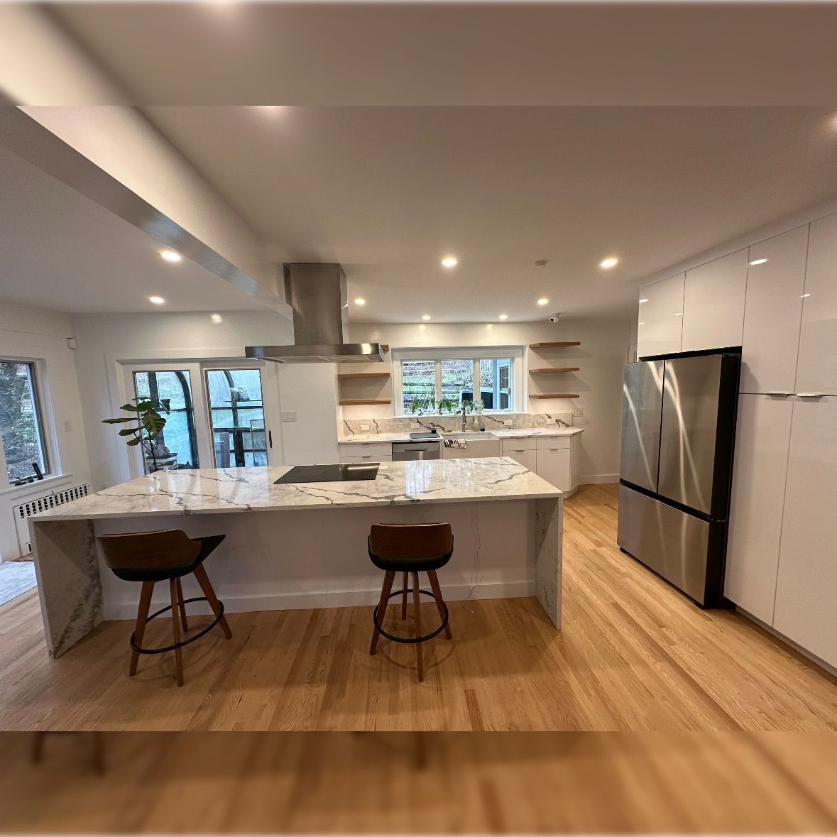Modern kitchen with white cabinets, marble island, stainless fridge, and two bar stools on wood floors