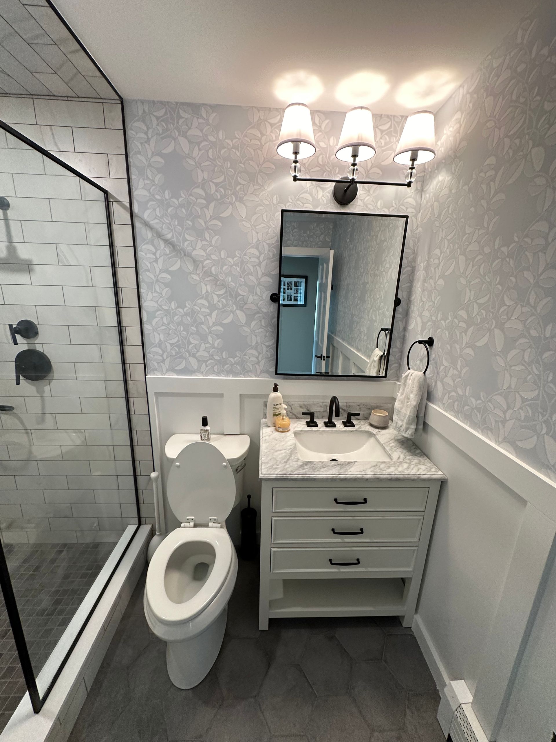 Small bathroom with glass shower, toilet, vanity sink, mirror, and wall sconces
