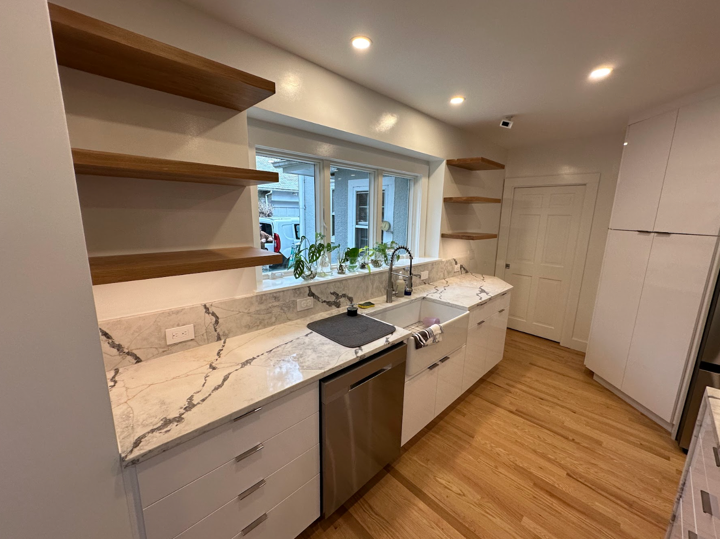 A kitchen with white cabinets , marble counter tops , stainless steel appliances and a large window.