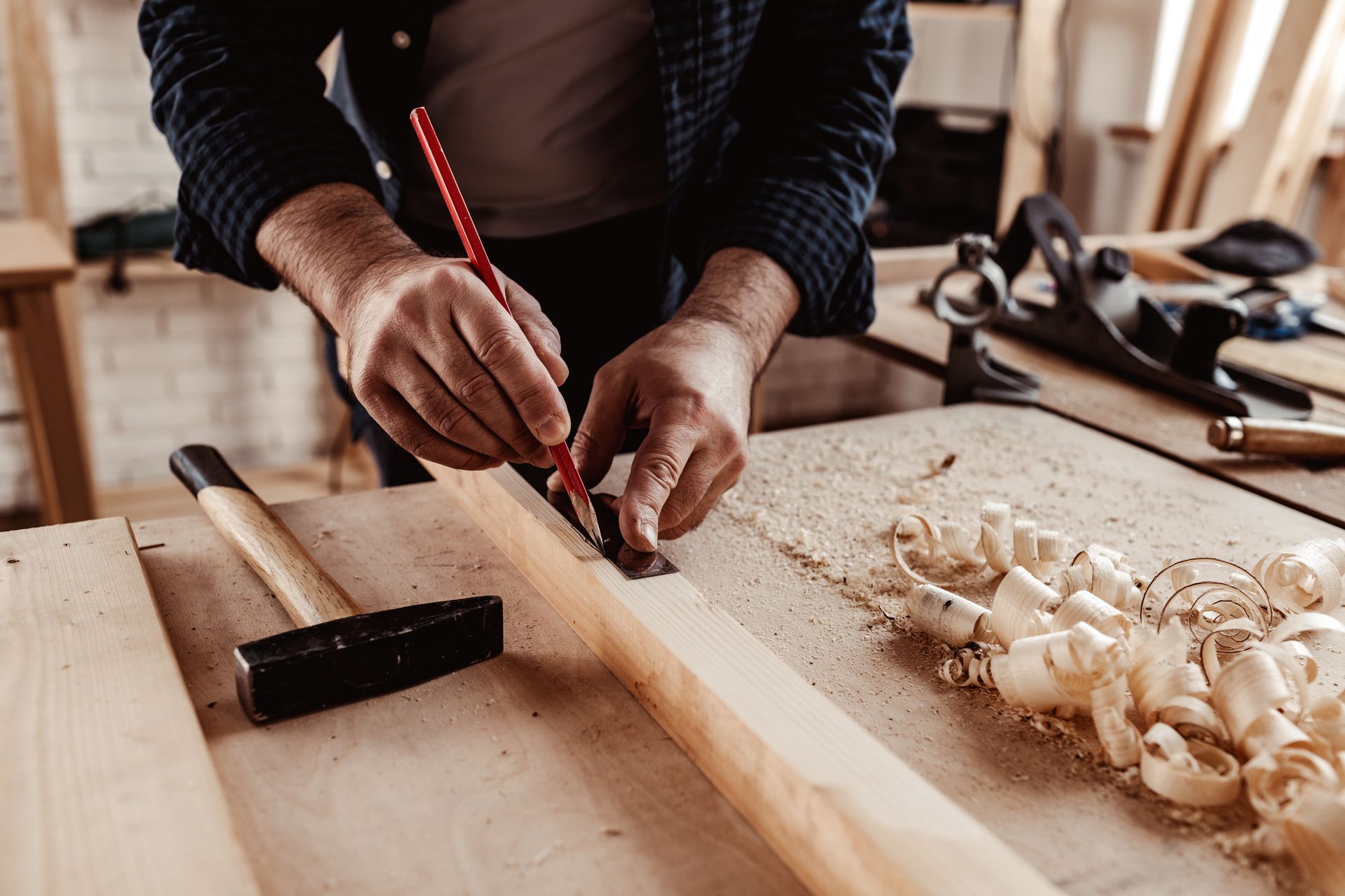 A man is measuring a piece of wood with a pencil.