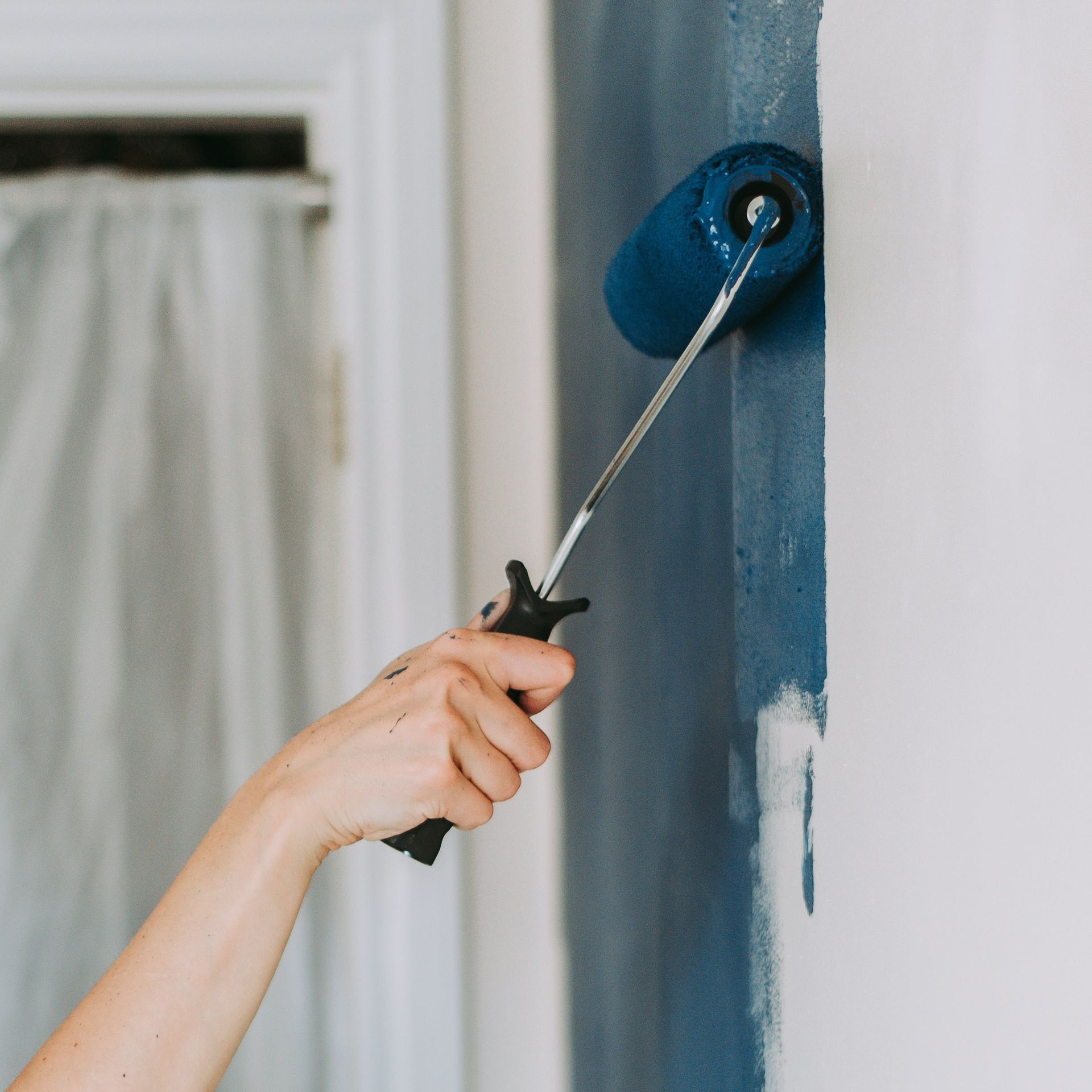 A person is painting a wall with a blue paint roller.