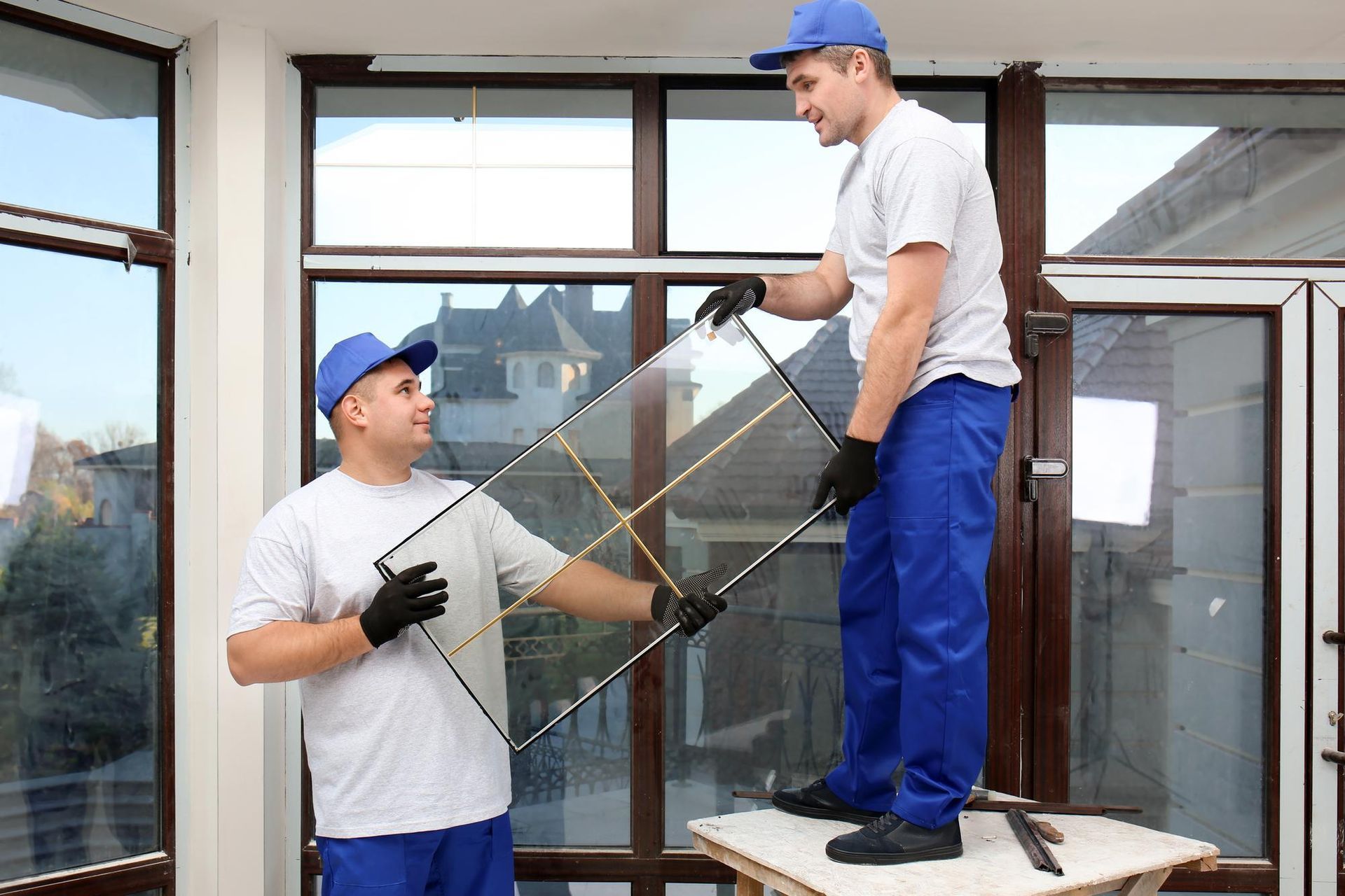 Two men are installing a glass window in a room.