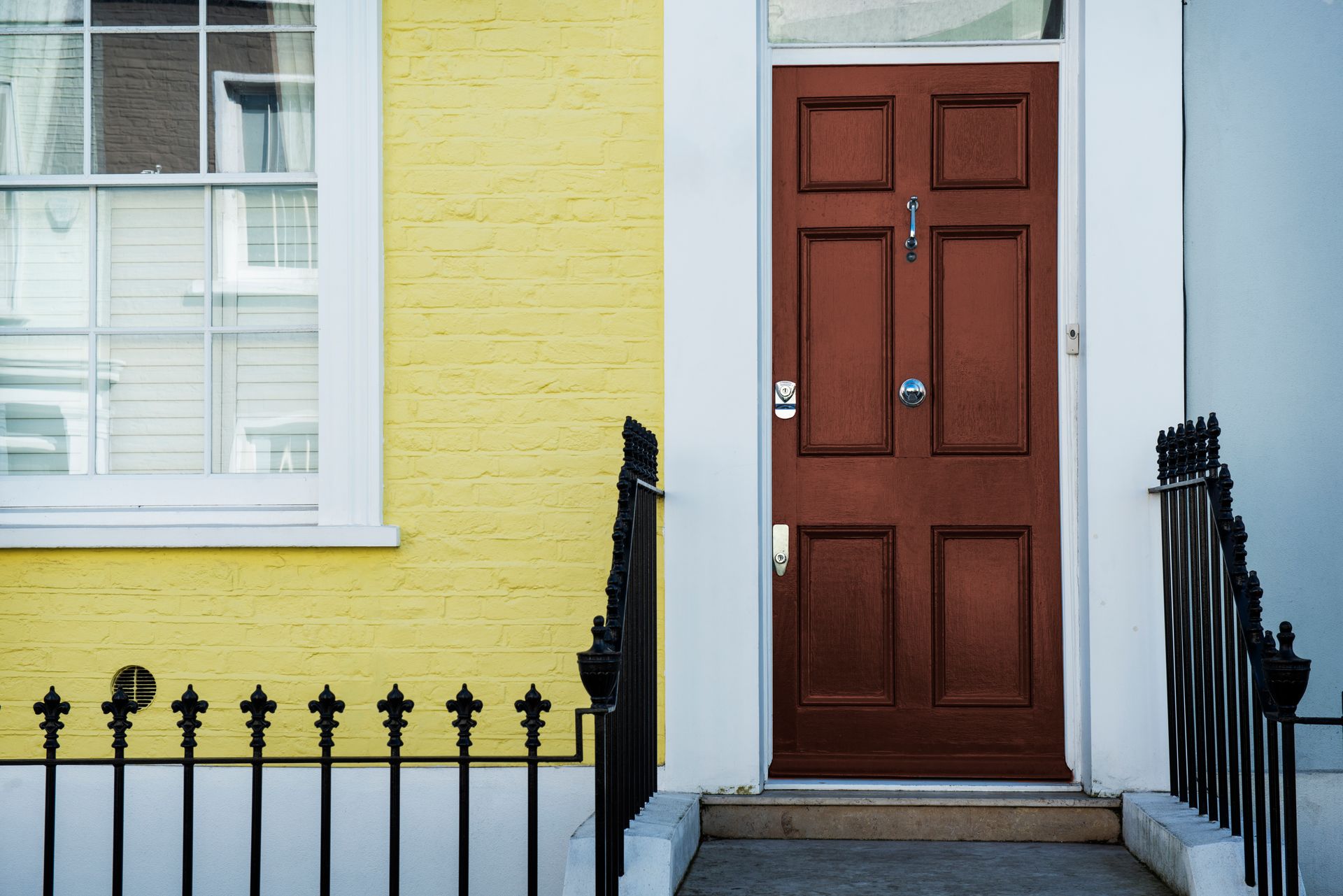 A yellow brick building with a red door and a black fence.