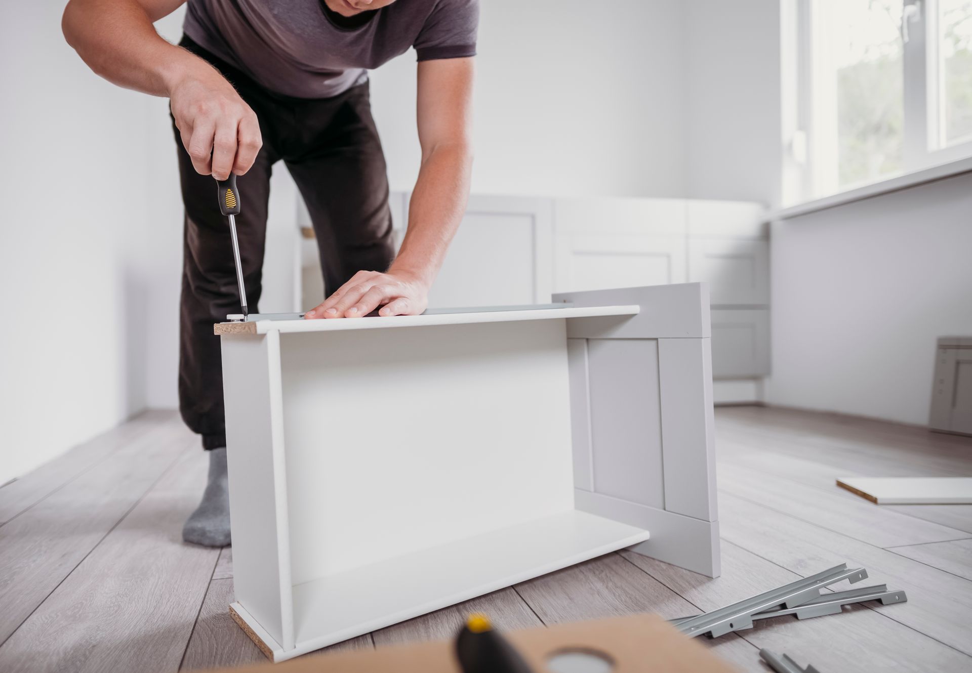 A man is using a screwdriver to fix a drawer in a kitchen.