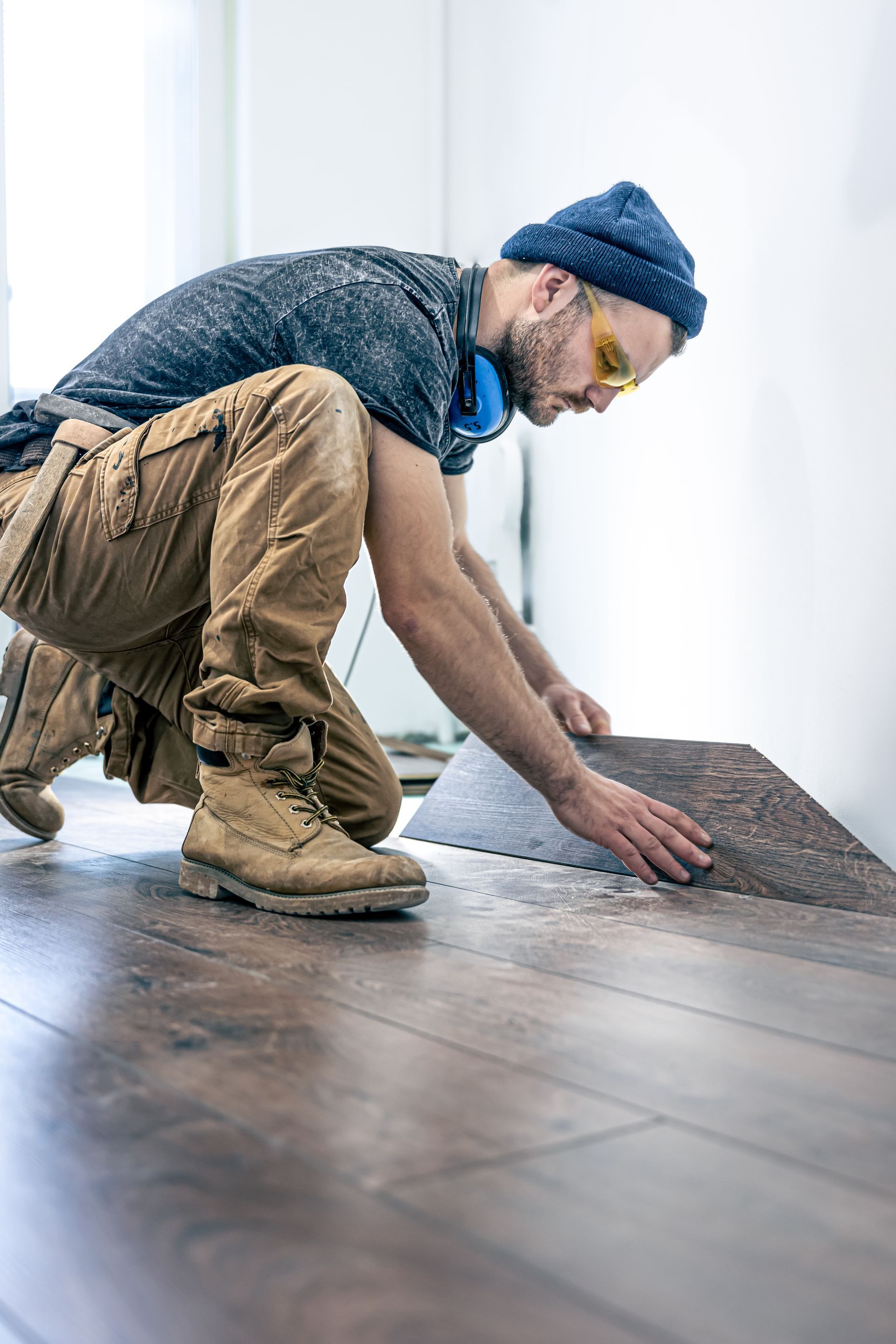 A man is installing a carpet on a wooden floor.