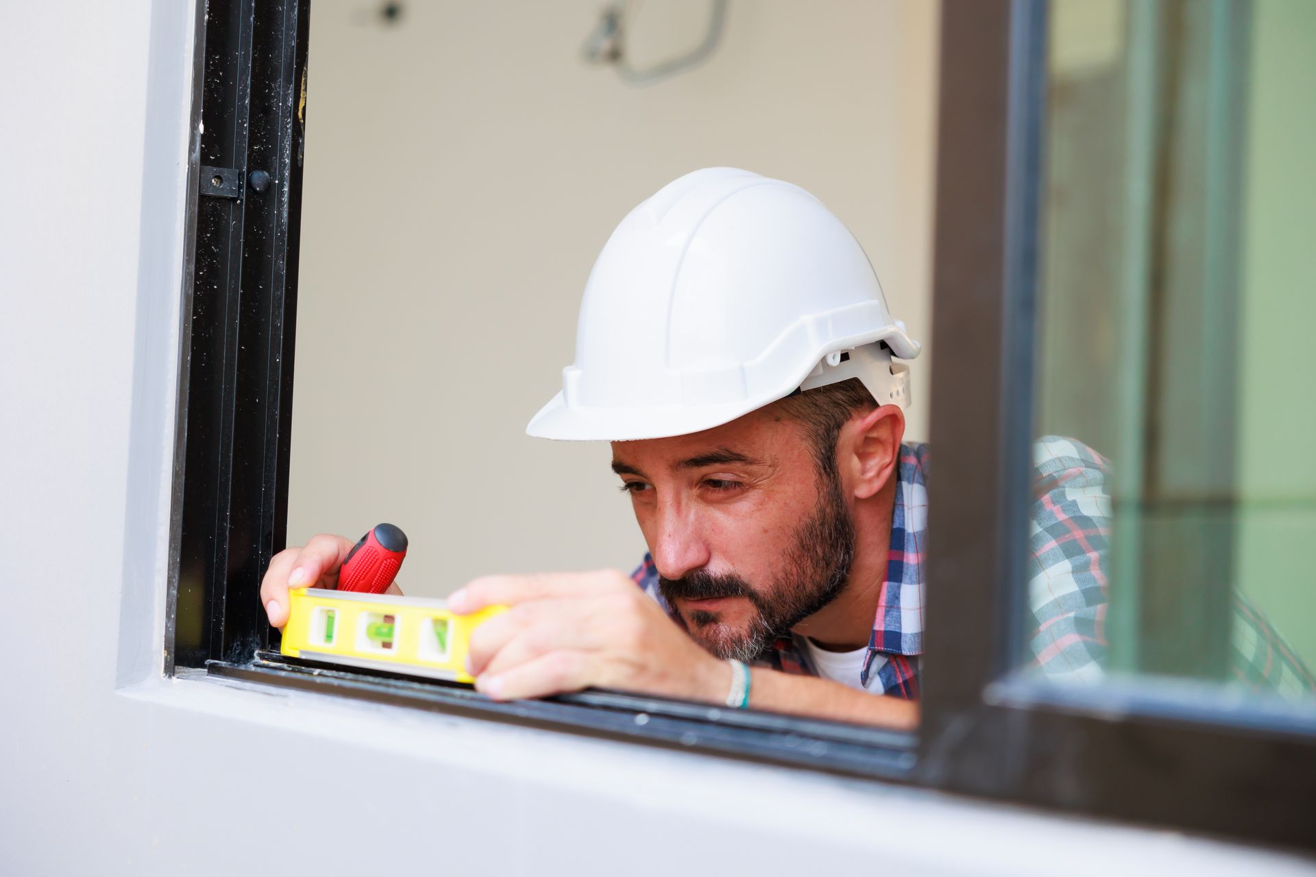 A man in a hard hat is measuring a window with a level.