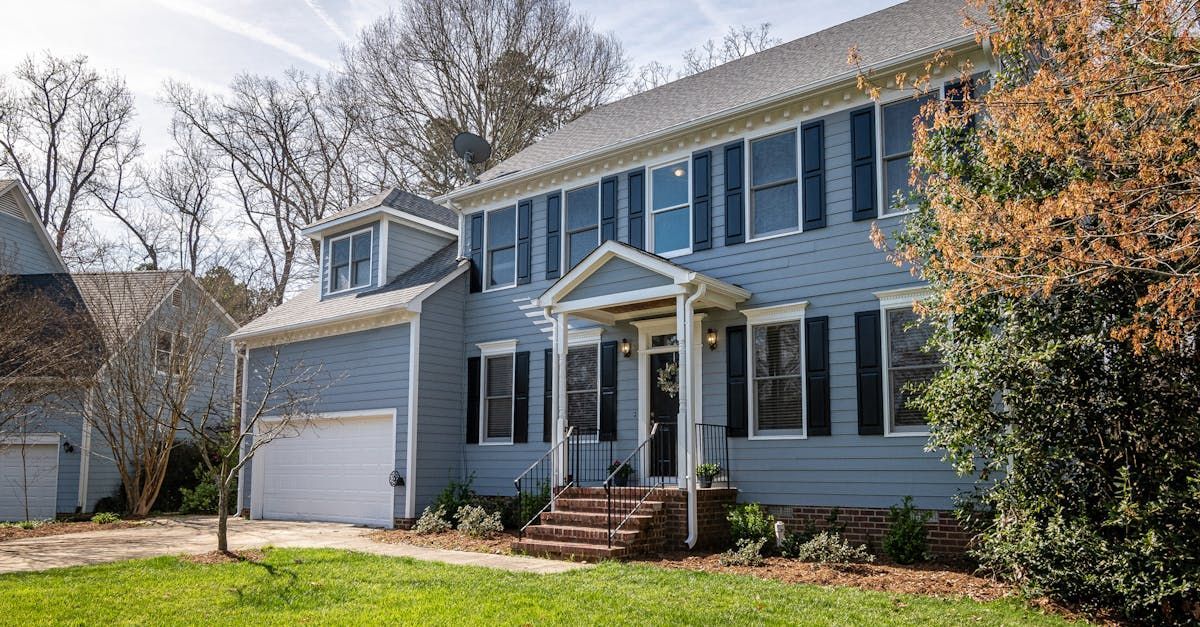 A large blue house with black shutters is sitting on top of a lush green lawn.