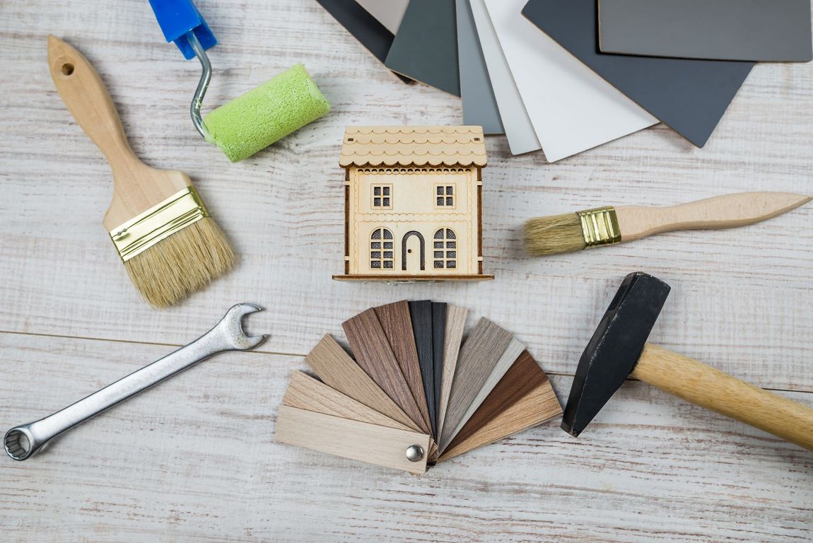 A wooden house is surrounded by paint brushes , a wrench , and a hammer.