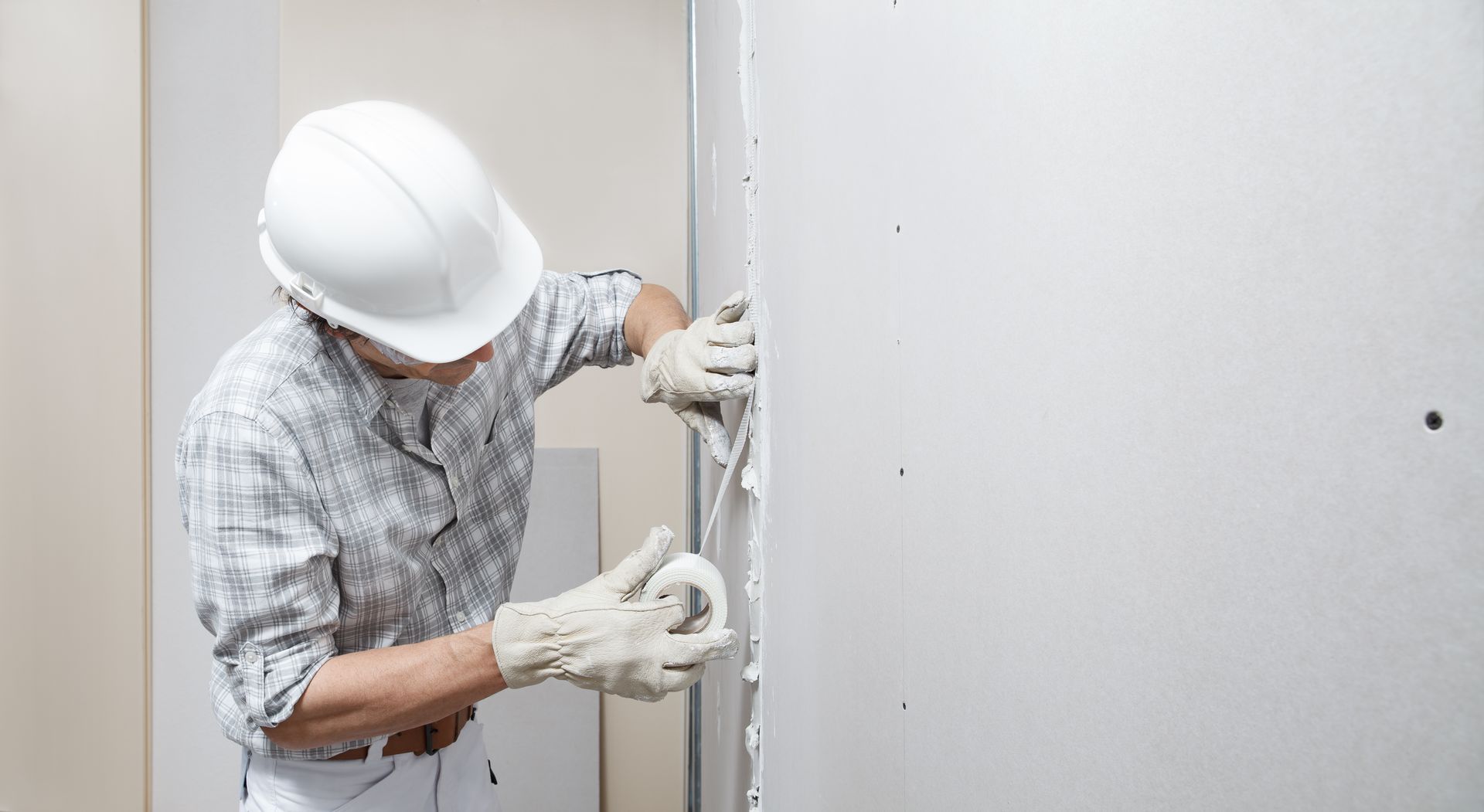 A man wearing a hard hat and gloves is plastering a wall.