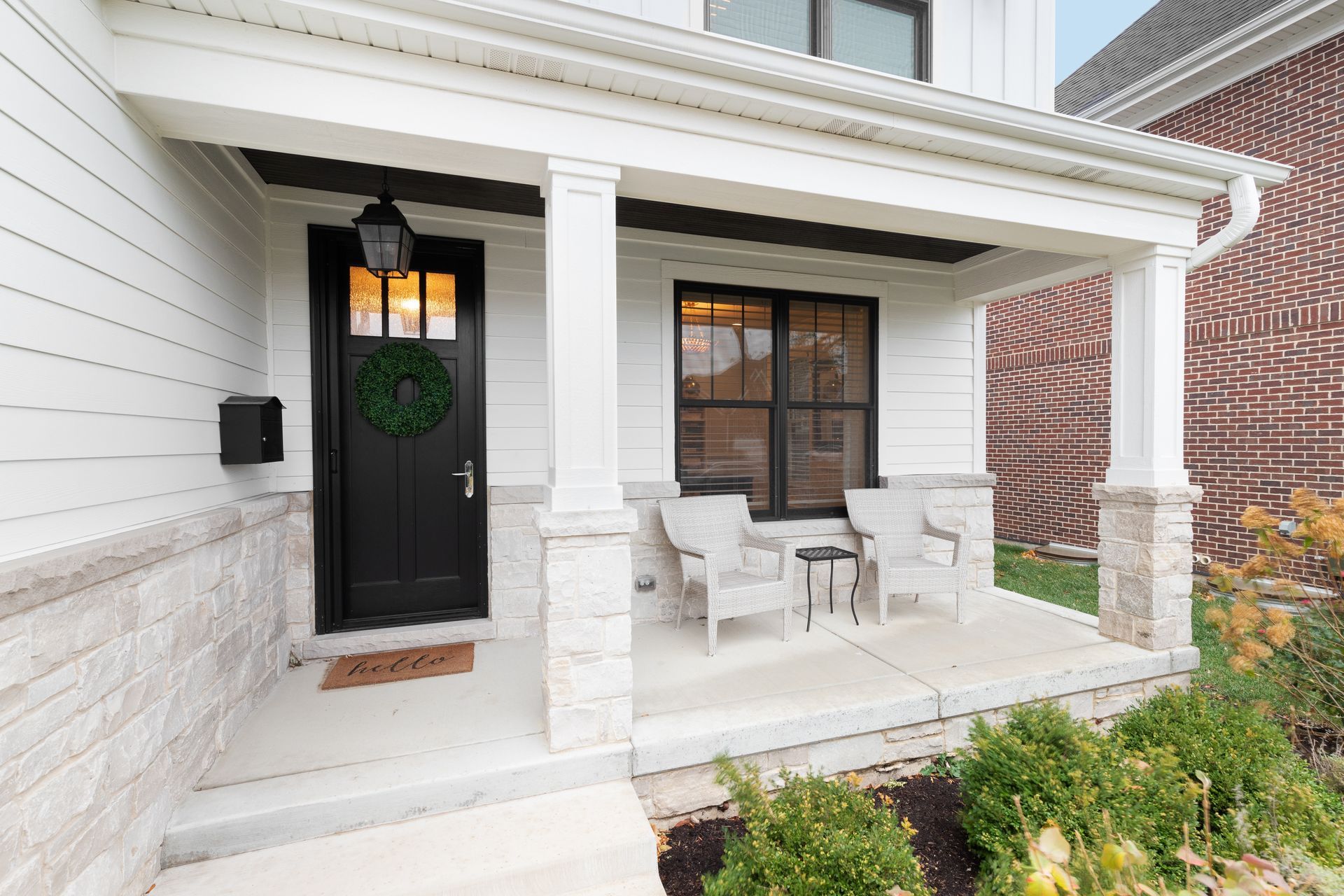 A white house with a black door and a porch with chairs and a table.