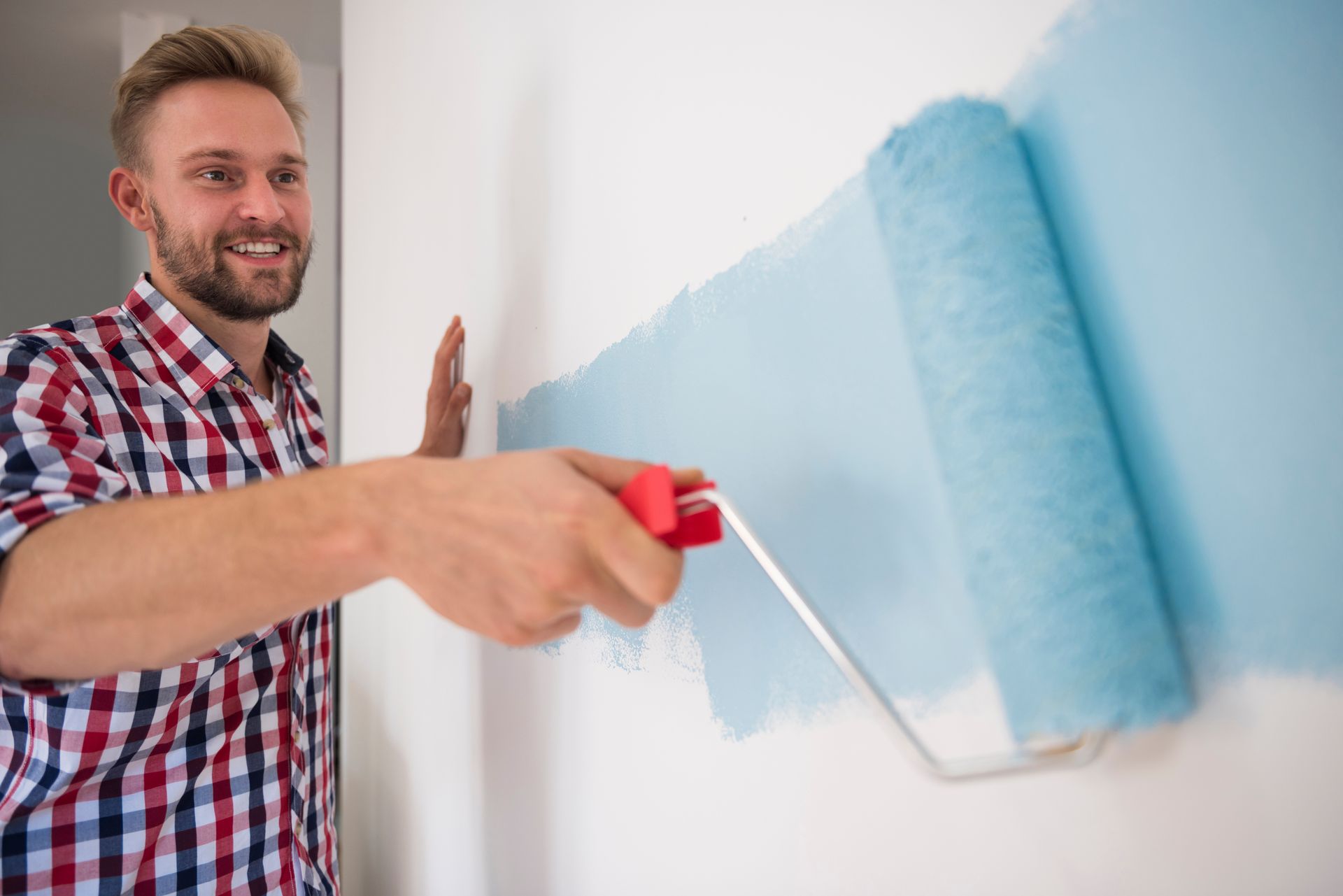 A man is painting a wall with a blue paint roller.