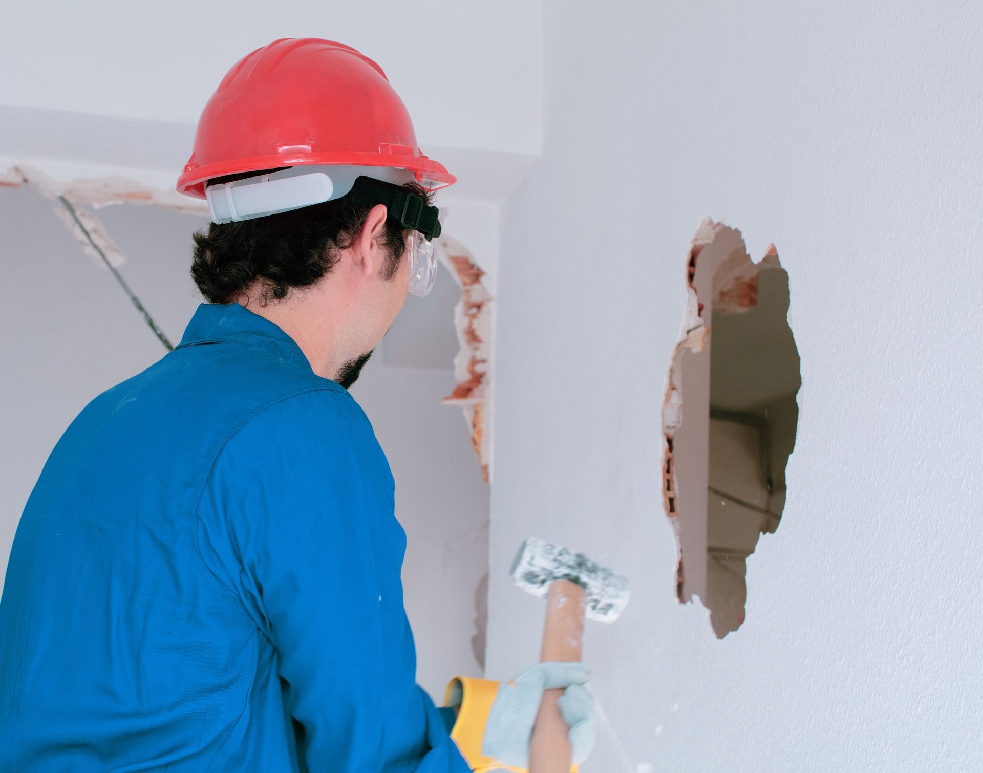 A man wearing a hard hat is plastering a hole in a wall.