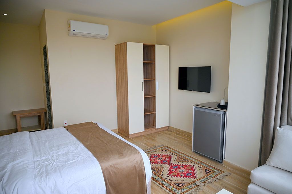 Bedroom with a bed, wardrobe, television, and small fridge. A decorative rug is on the floor.
