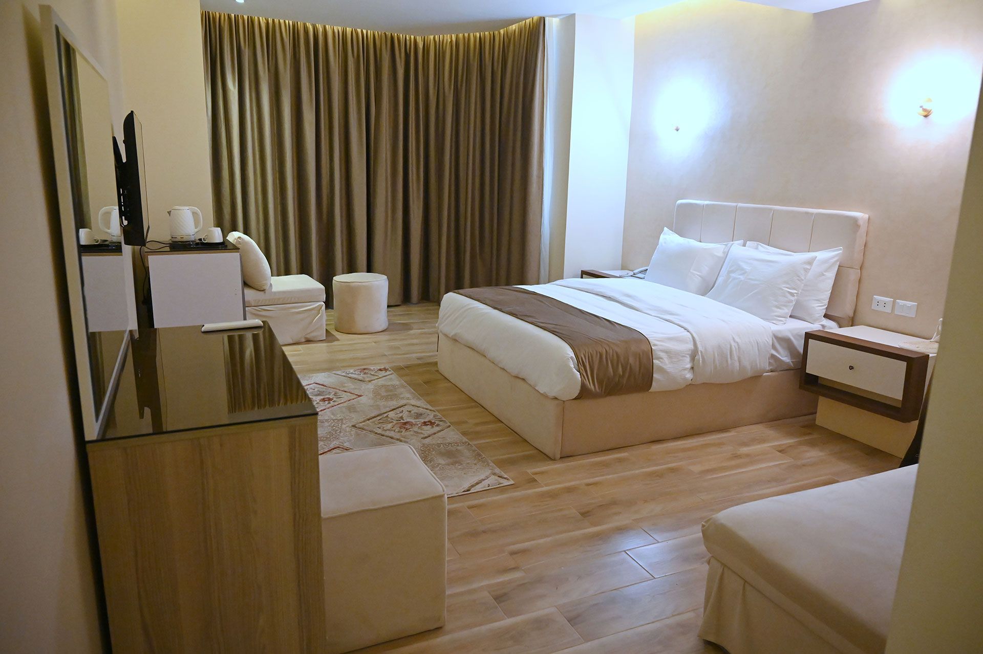 Hotel room with bed, dresser, and armchair. Beige and brown color scheme with wooden floors.