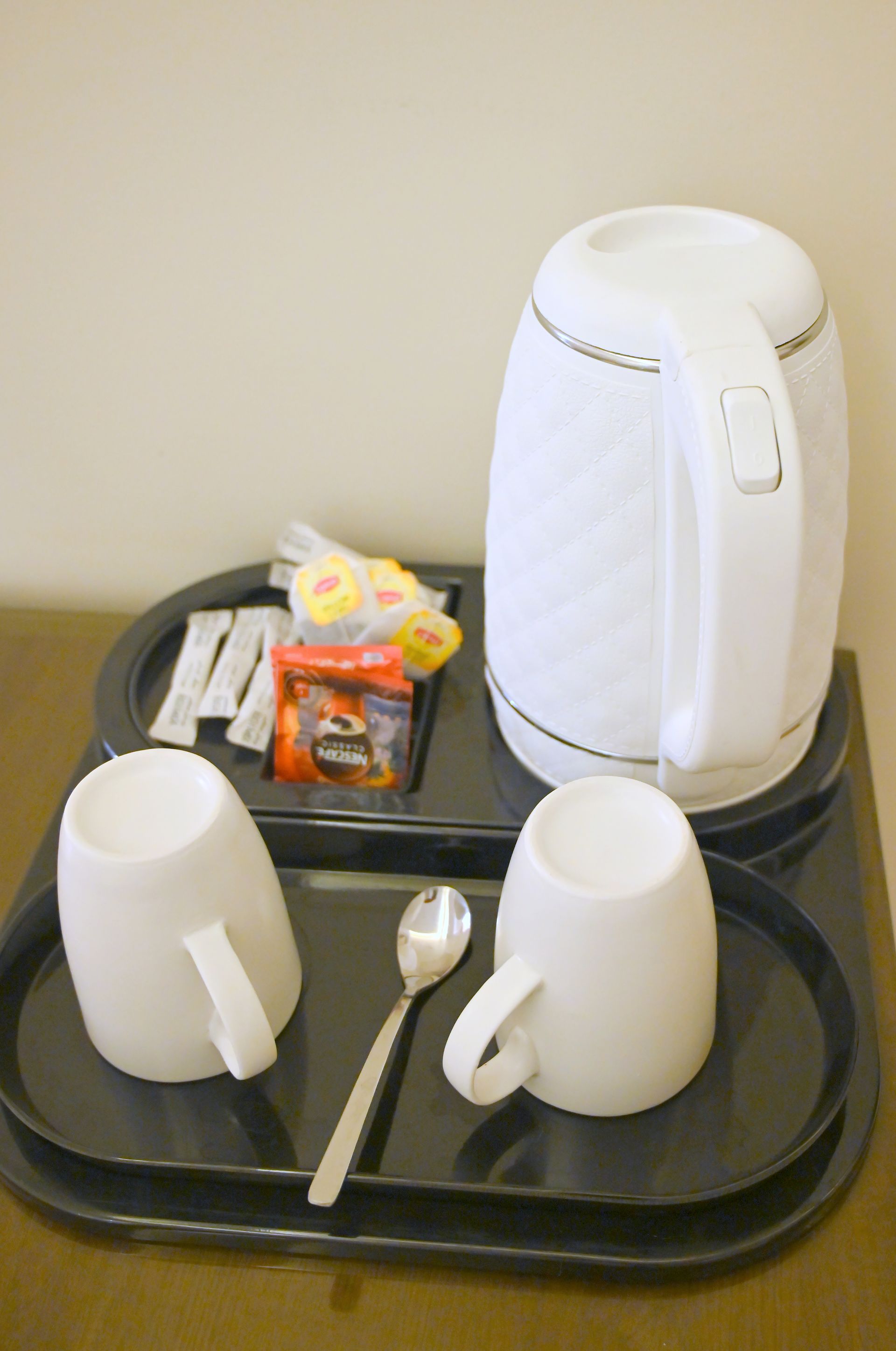 White electric kettle and mugs on a tray with tea and sugar packets.