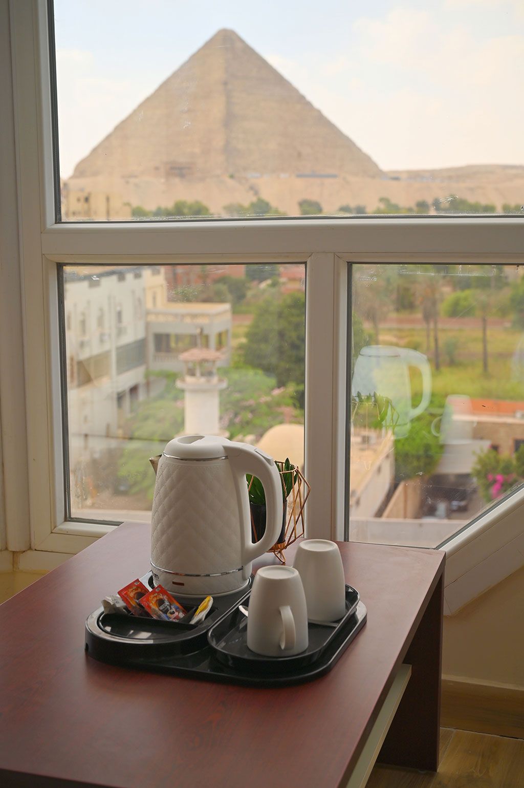 Tea set on table with Great Pyramid of Giza visible through window.