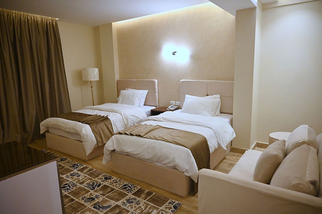 Twin hotel room with two beds, small couch, neutral colors, and area rug.