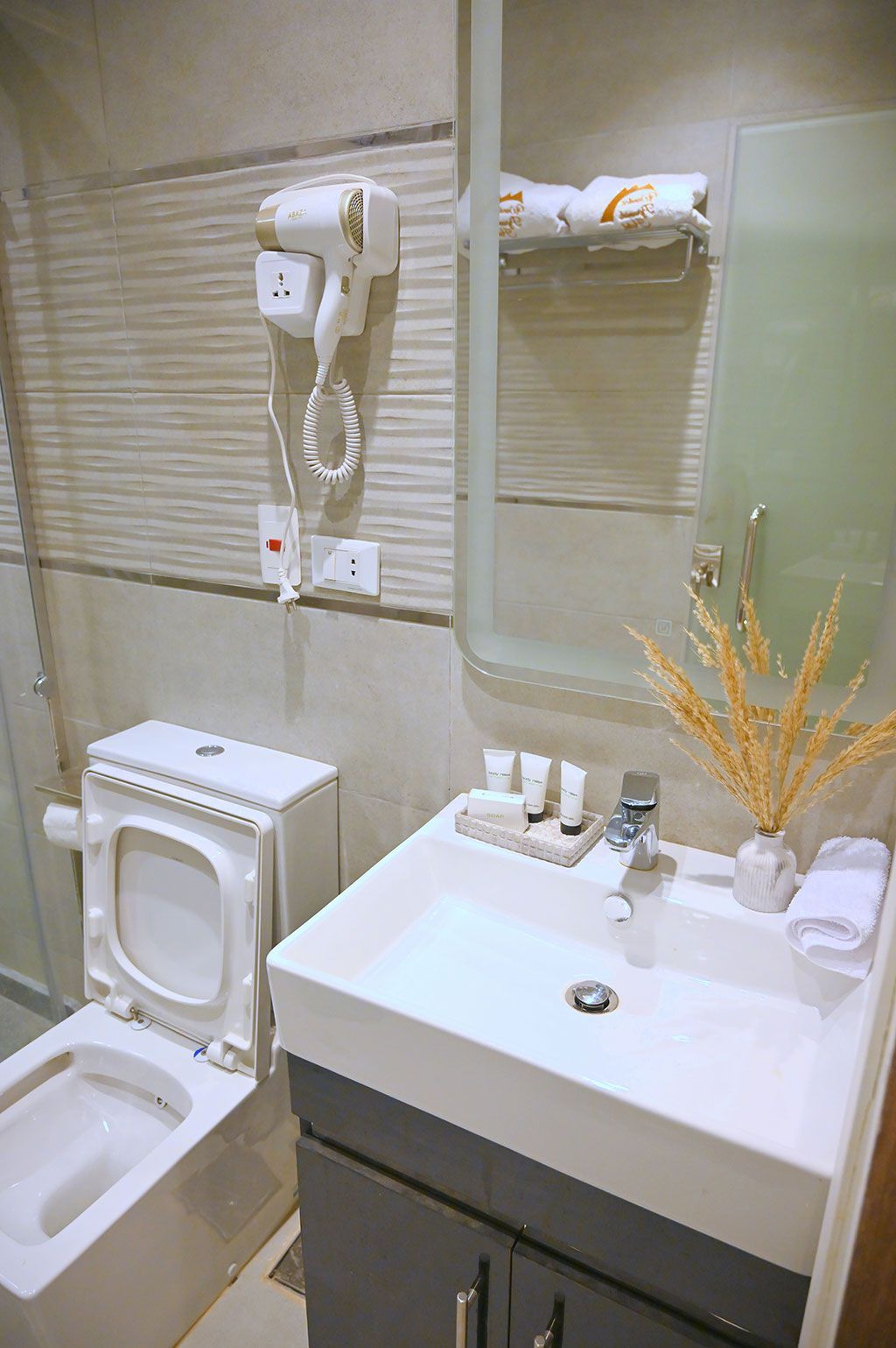 Bathroom with toilet, sink, mirror, hairdryer, and towels; neutral colors.