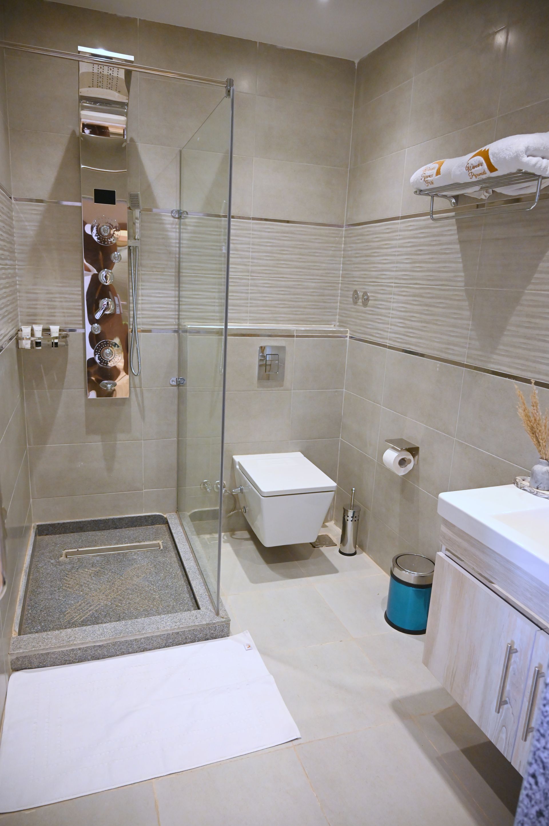 Bathroom with walk-in shower, wall-mounted toilet, vanity, and neutral-toned tiles.