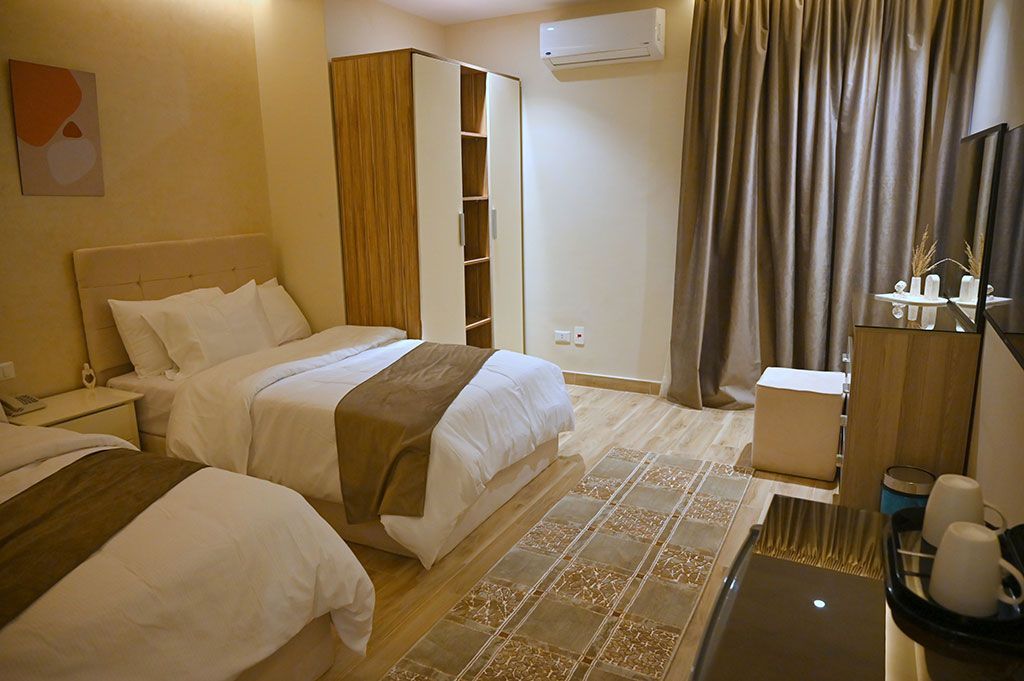A hotel room with two twin beds, a wooden closet, curtains, and a small table.