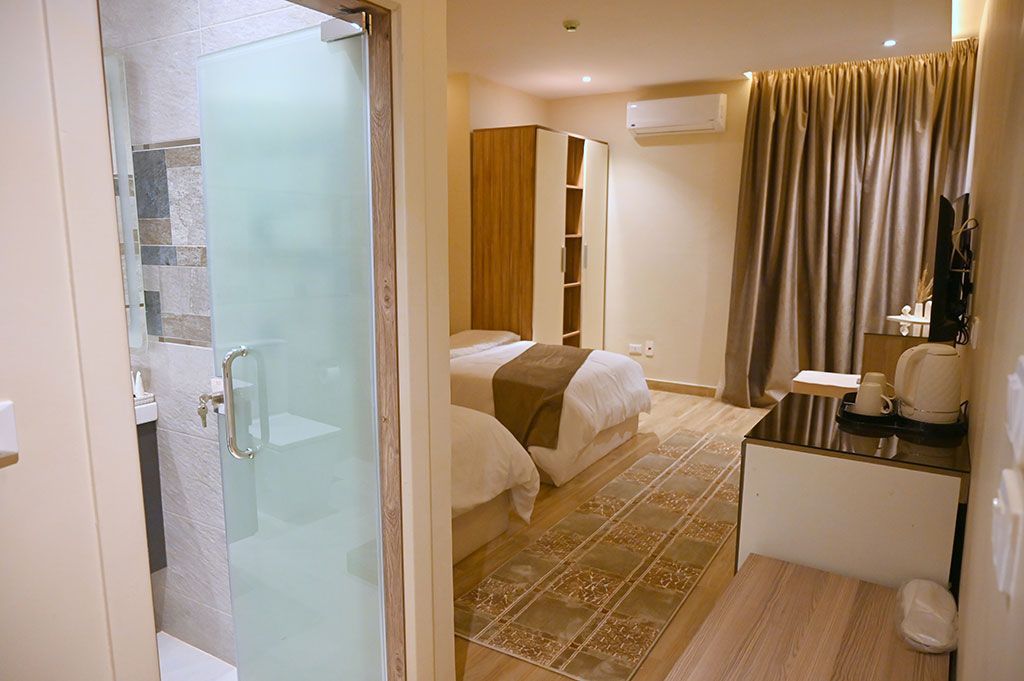 Hotel room with twin beds, bathroom with frosted glass door, beige walls, and brown curtains.