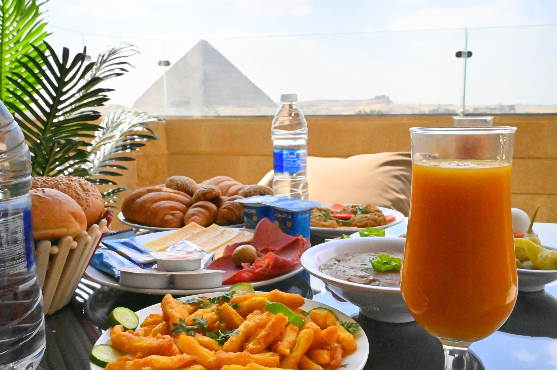 Breakfast spread on a table overlooking a pyramid. Includes pastries, fruit, juice, and other dishes.