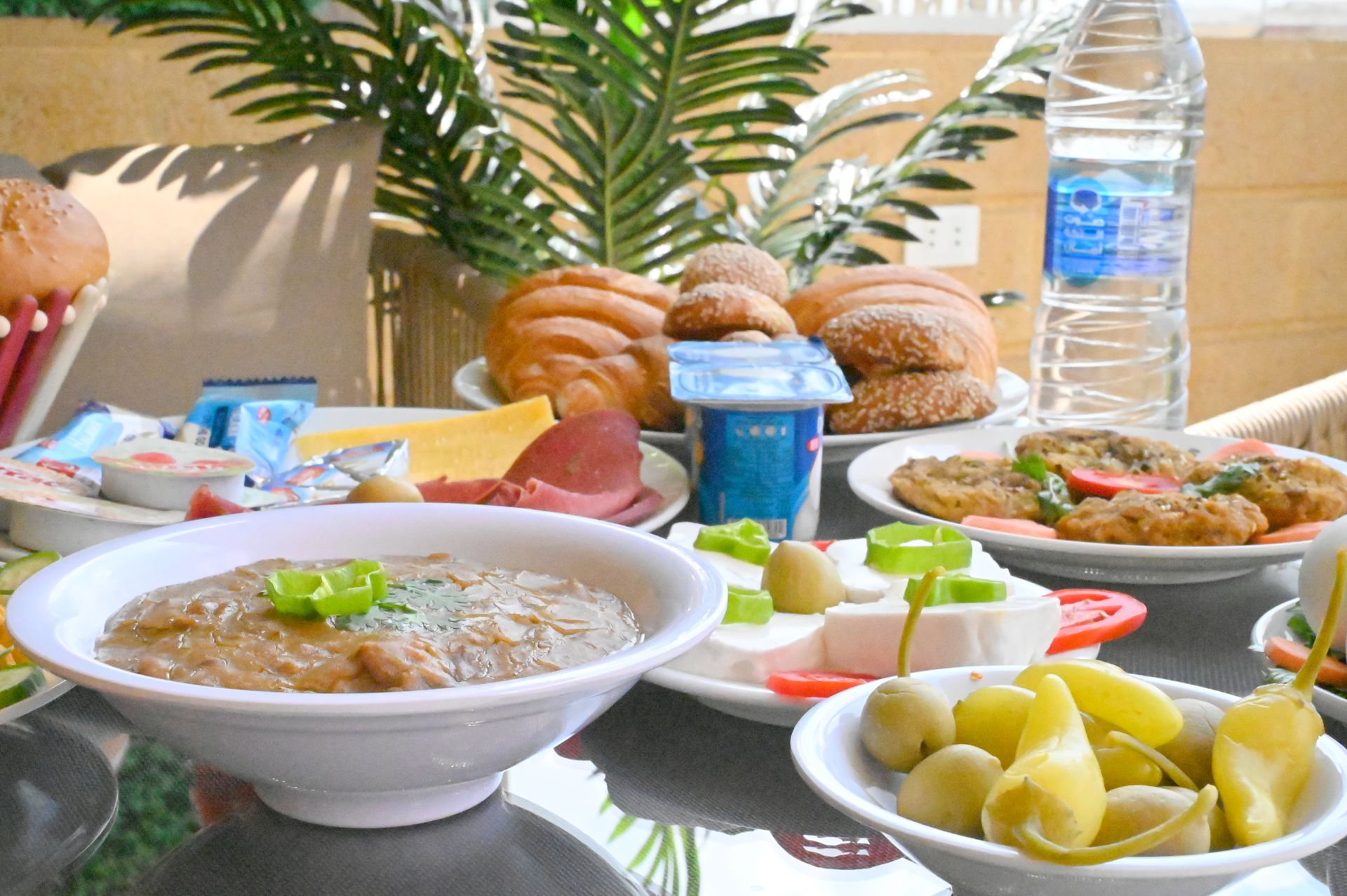 Breakfast spread with bread, eggs, cheese, olives, yogurt, and water on a table.