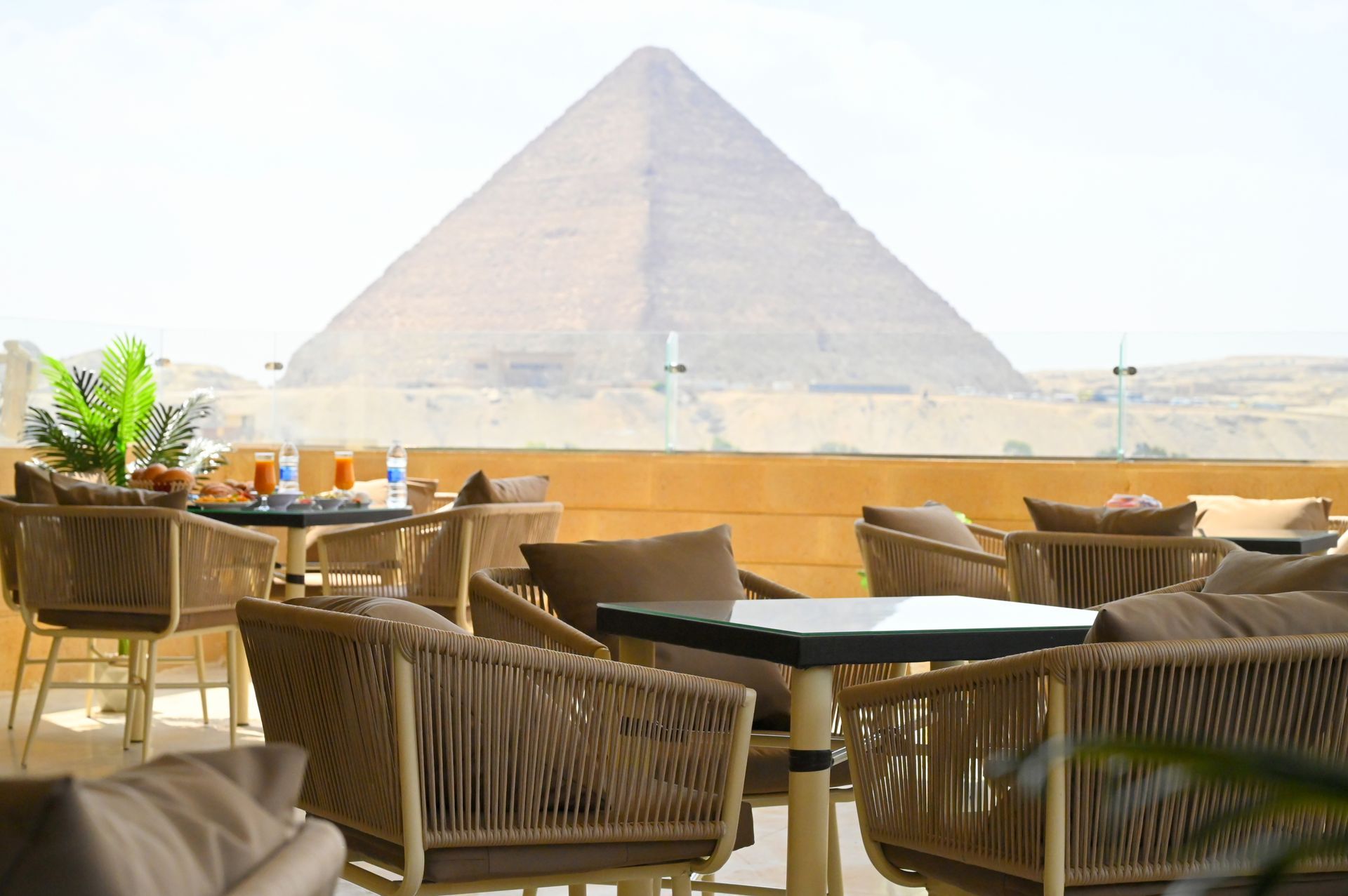 Restaurant patio with Great Pyramid in background. Wicker chairs, tables, and food visible. Sunny day.