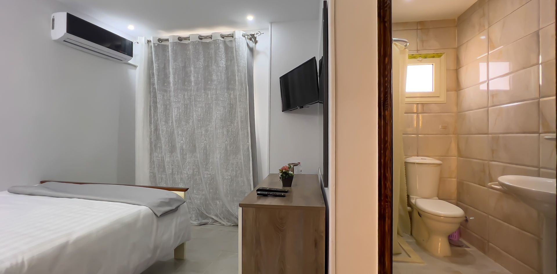 Bedroom interior with a bed, air conditioner, TV, and open doorway to a bathroom.