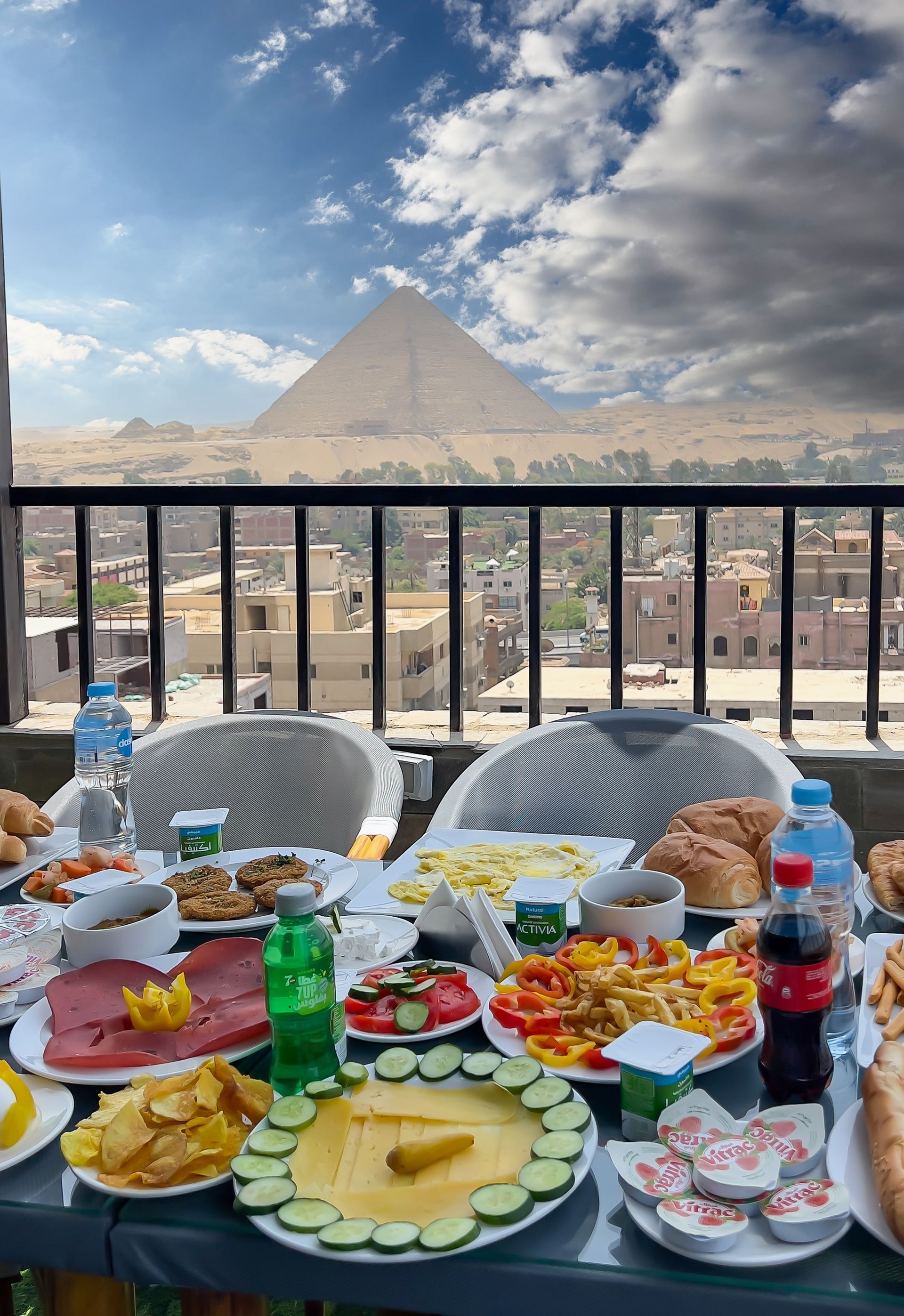 A table laden with food, overlooking the pyramids in Egypt, under a cloudy sky.