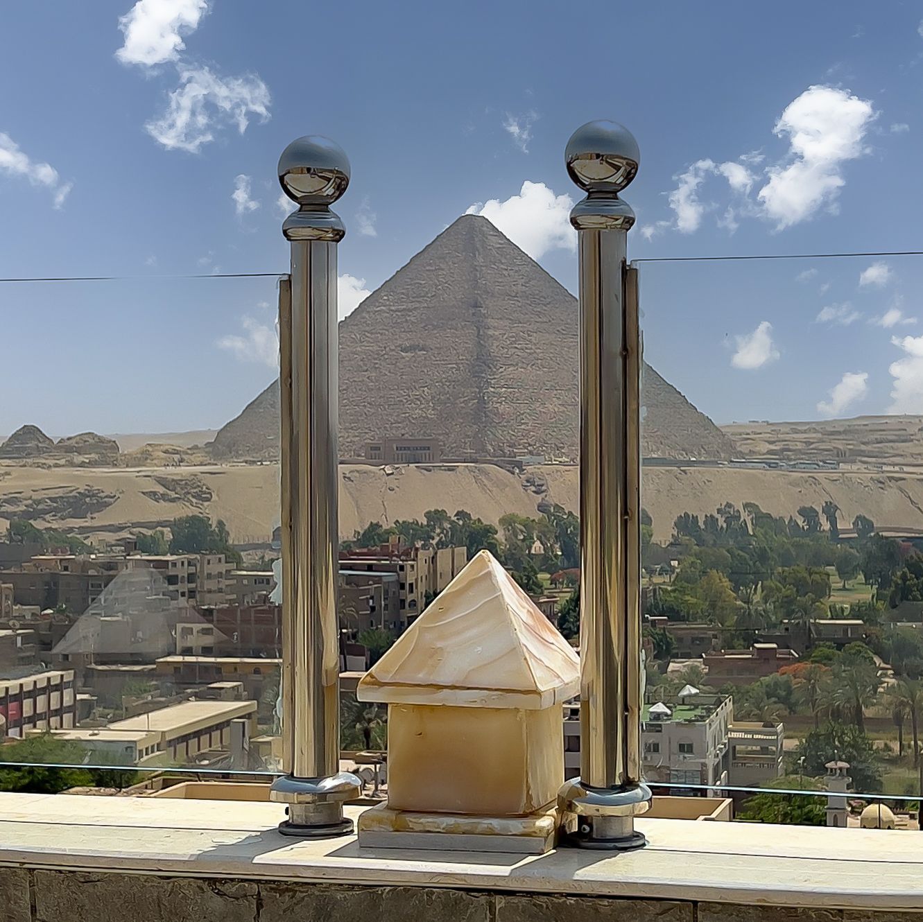 Two silver posts with a small pyramid in front, Great Pyramid of Giza in the background, blue sky.
