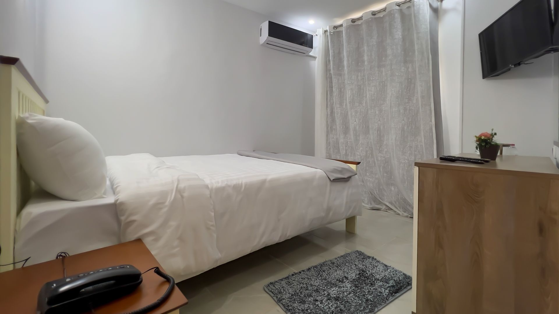Bedroom with bed, bedside table with phone, dresser, AC unit, and patterned curtains.